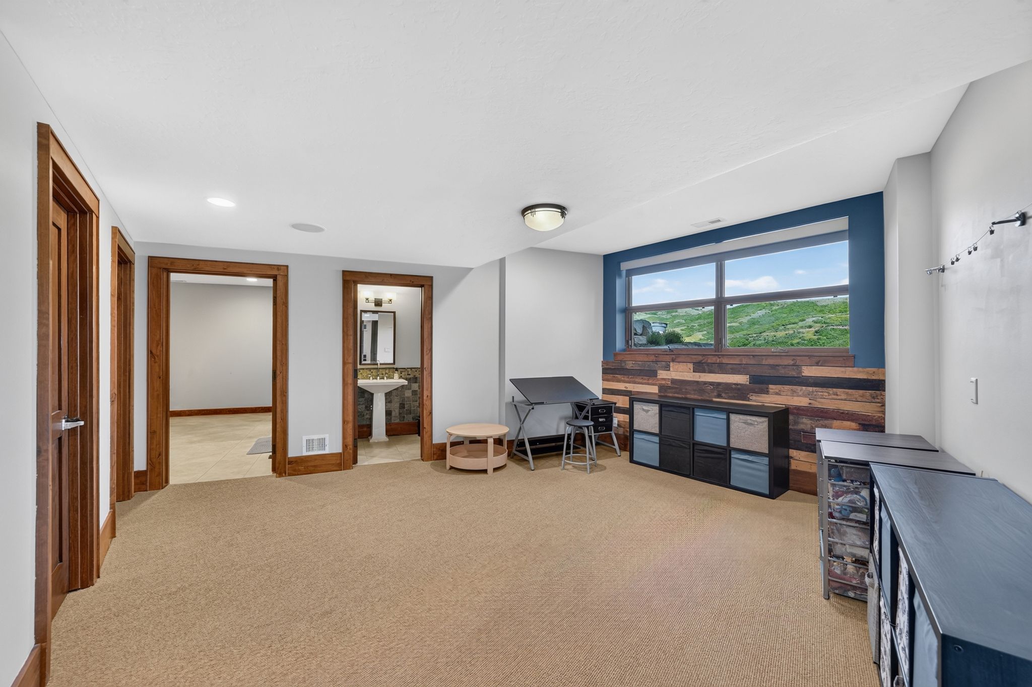 Spacious room featuring carpeted flooring, a large window with a landscape backdrop, and a wood-paneled accent wall