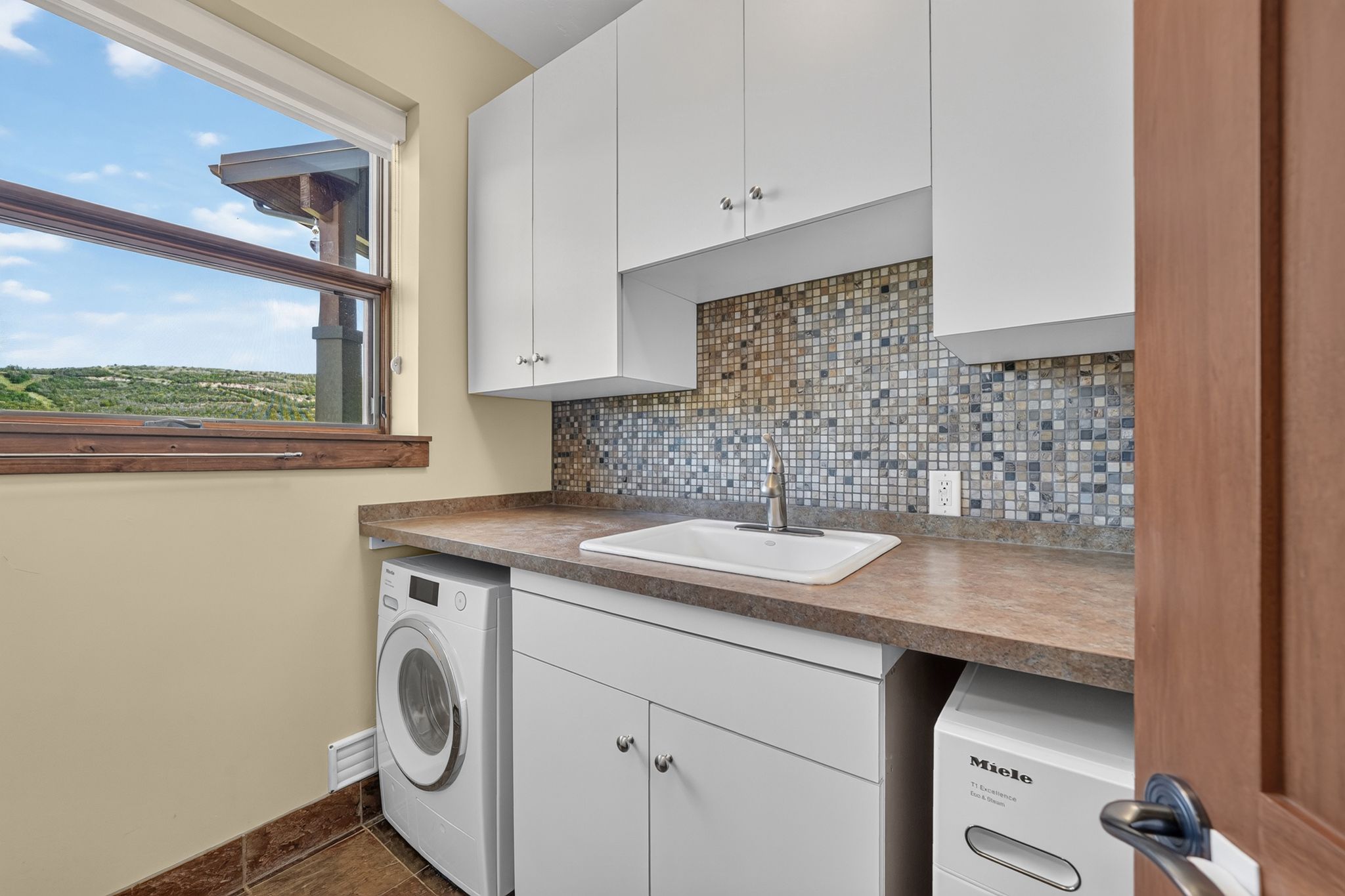 Laundry area with ample white cabinetry, integrated sink, and a multi-tone mosaic tile backsplash