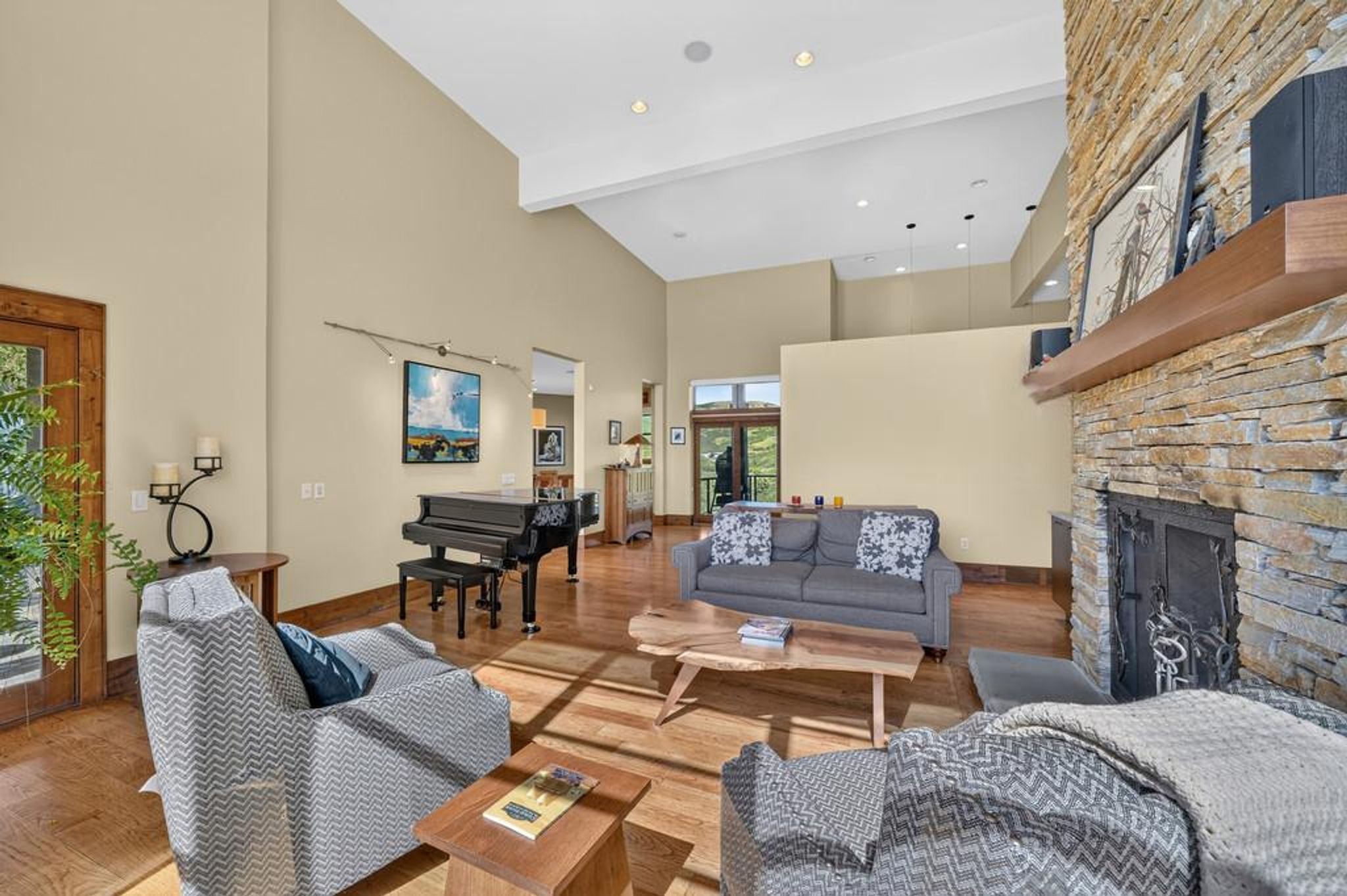 Grand living room featuring a stacked stone fireplace with a substantial wood mantel, vaulted ceilings, recessed lighting, and hardwood flooring