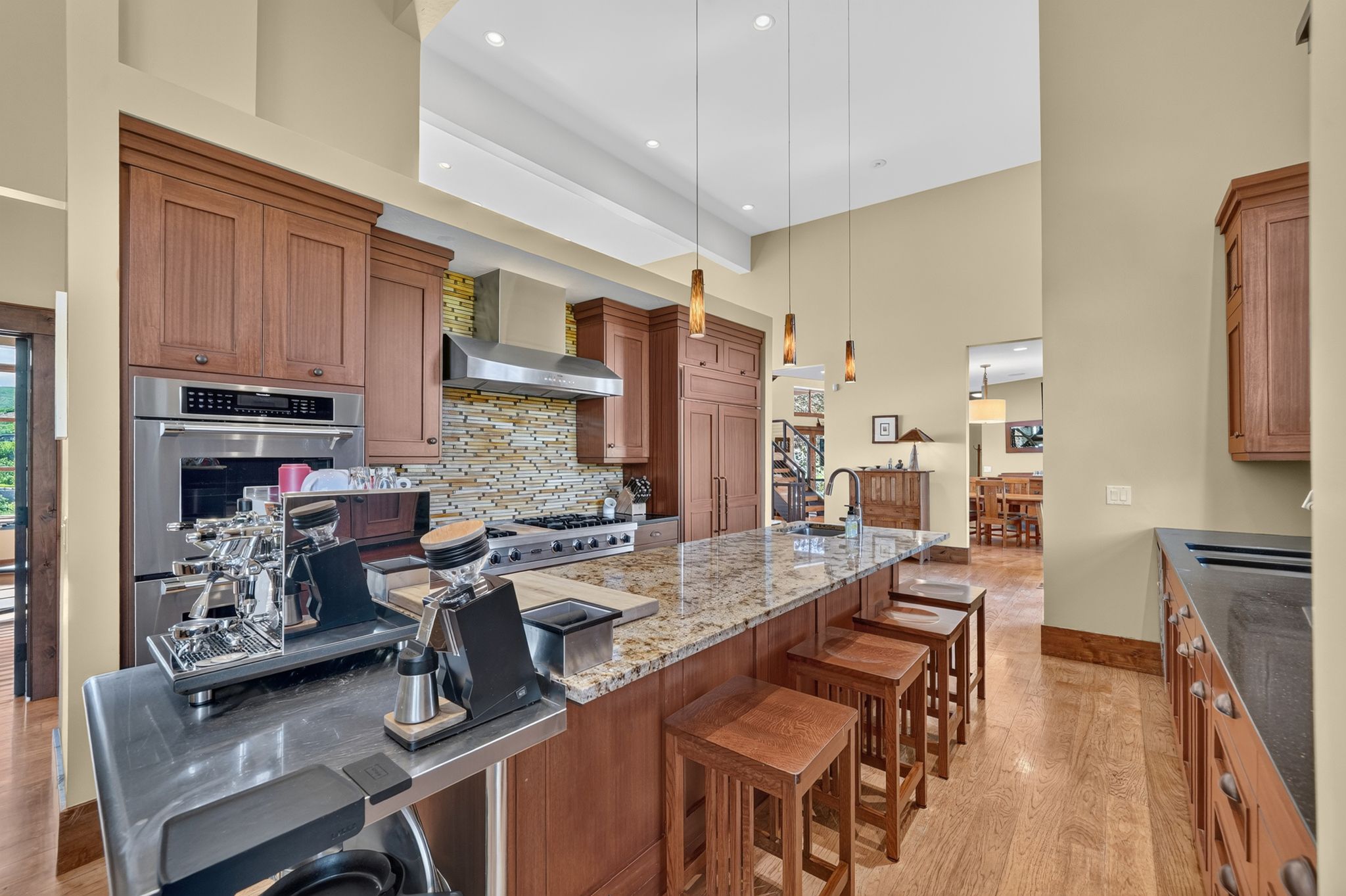 Gourmet kitchen featuring a substantial island with stone countertop, stainless steel appliances, a stone tile backsplash, and light wood-finish flooring