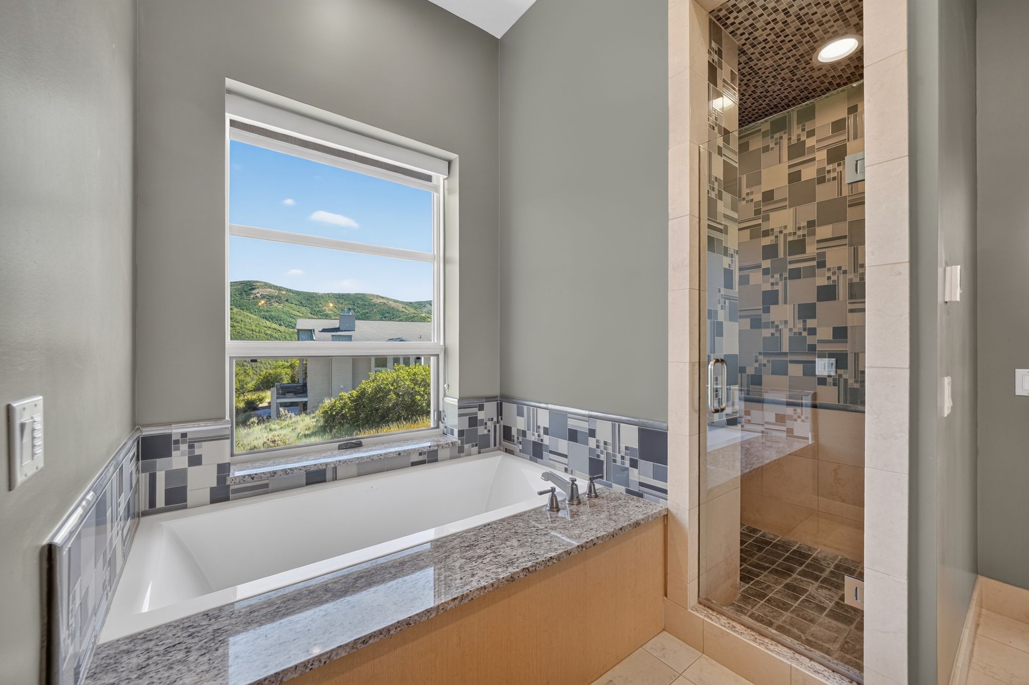 Soaking tub with a granite surround, complemented by a mosaic tile backsplash