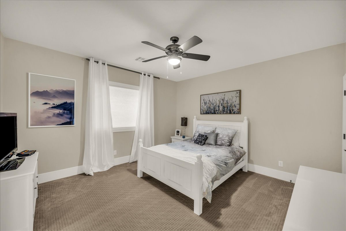 Spacious room featuring neutral-toned walls, plush carpeting, a large window, a ceiling fan with integrated lighting, and white baseboards