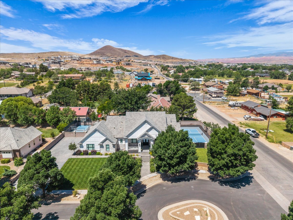 Expansive property featuring a contemporary residence with a grey roof, a manicured front lawn, mature trees, a private tennis court, and a paved driveway