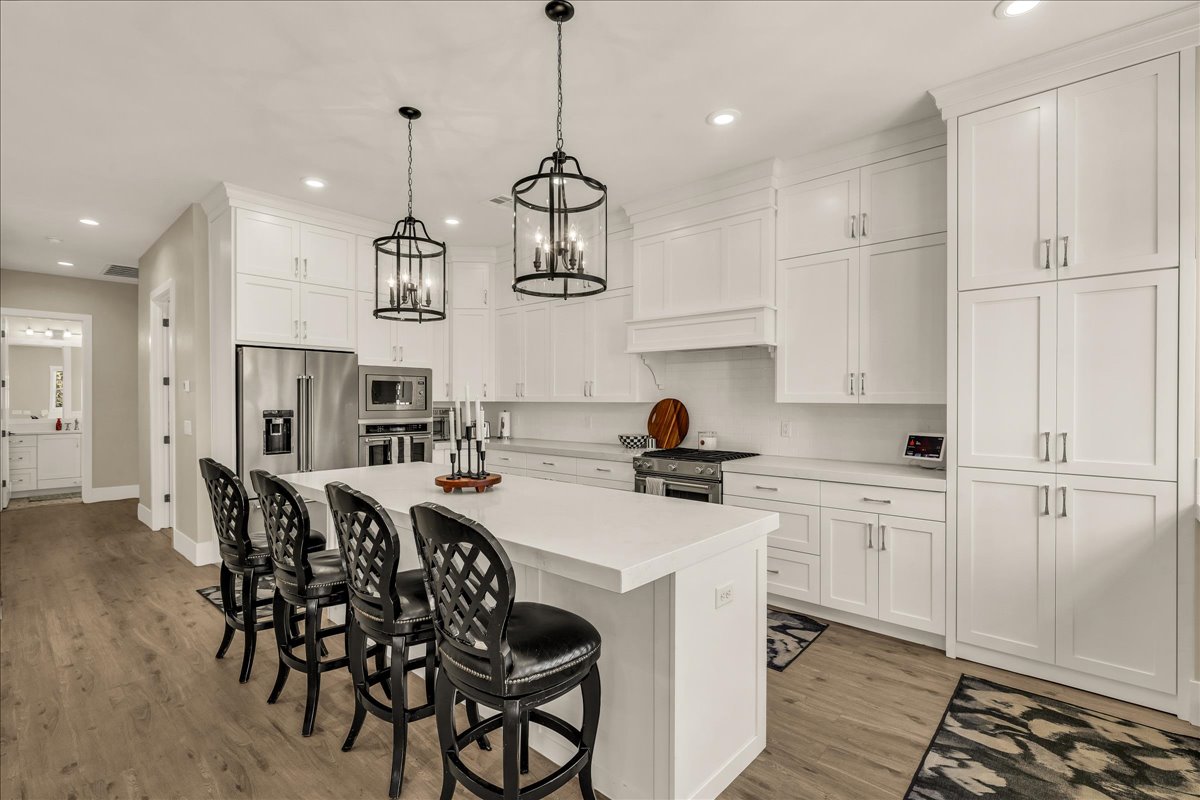 Spacious kitchen featuring an expansive central island with seating, extensive white cabinetry, light-toned countertops, stainless steel appliances, and wood-finish flooring