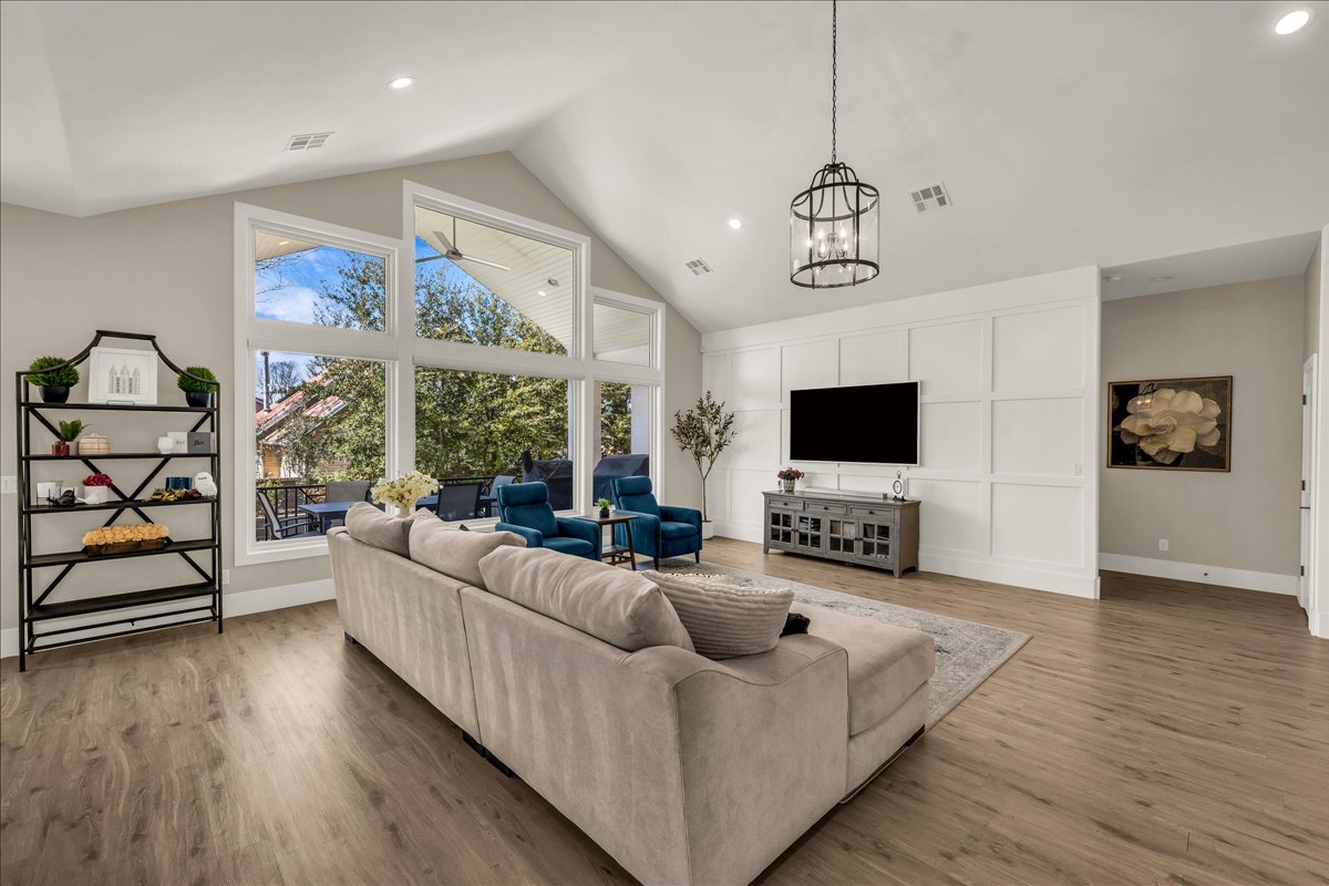 Spacious living area featuring vaulted ceilings, expansive window wall, wood-finish flooring, and a modern paneled accent wall with a hanging light fixture