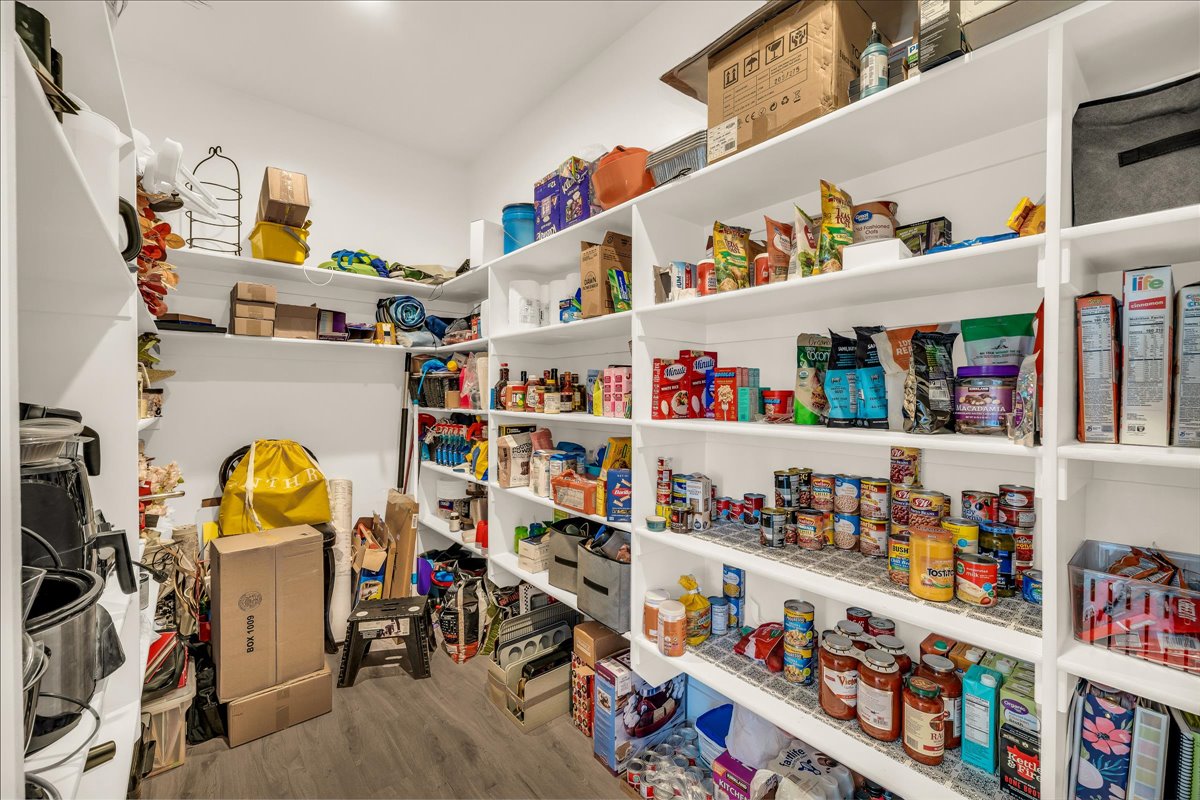 Spacious walk-in pantry featuring extensive white shelving, wood-finish flooring, and ample storage capacity