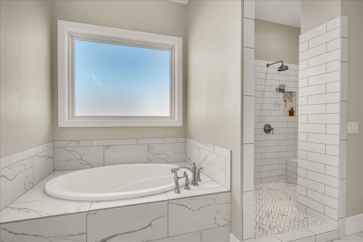 Built-in soaking tub with deck-mounted fixtures, surrounded by large format tile with a marble-effect finish