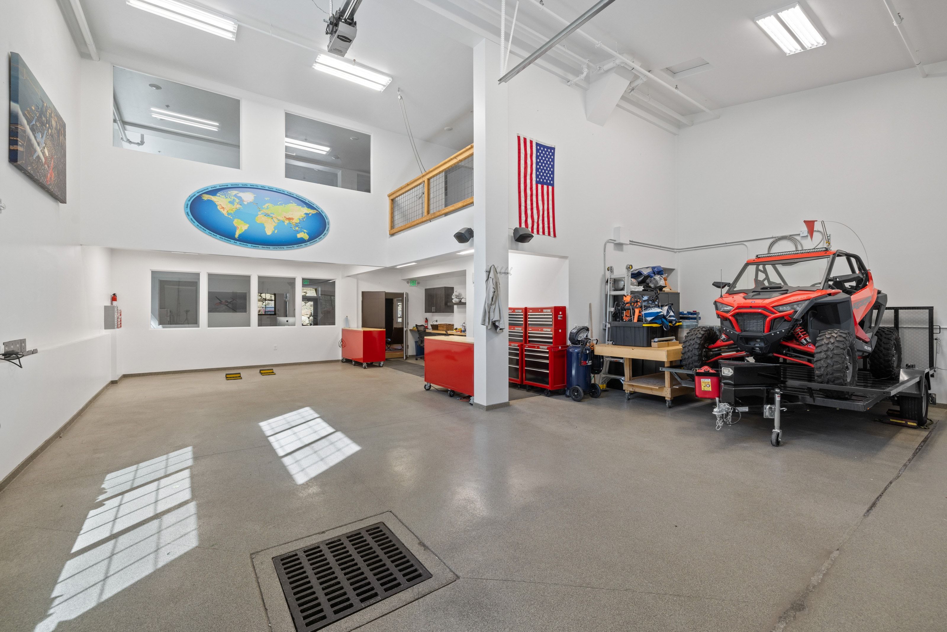Spacious garage with high ceilings, polished concrete flooring, extensive built-in lighting, an integrated floor drain, and multiple wall-mounted windows providing natural illumination