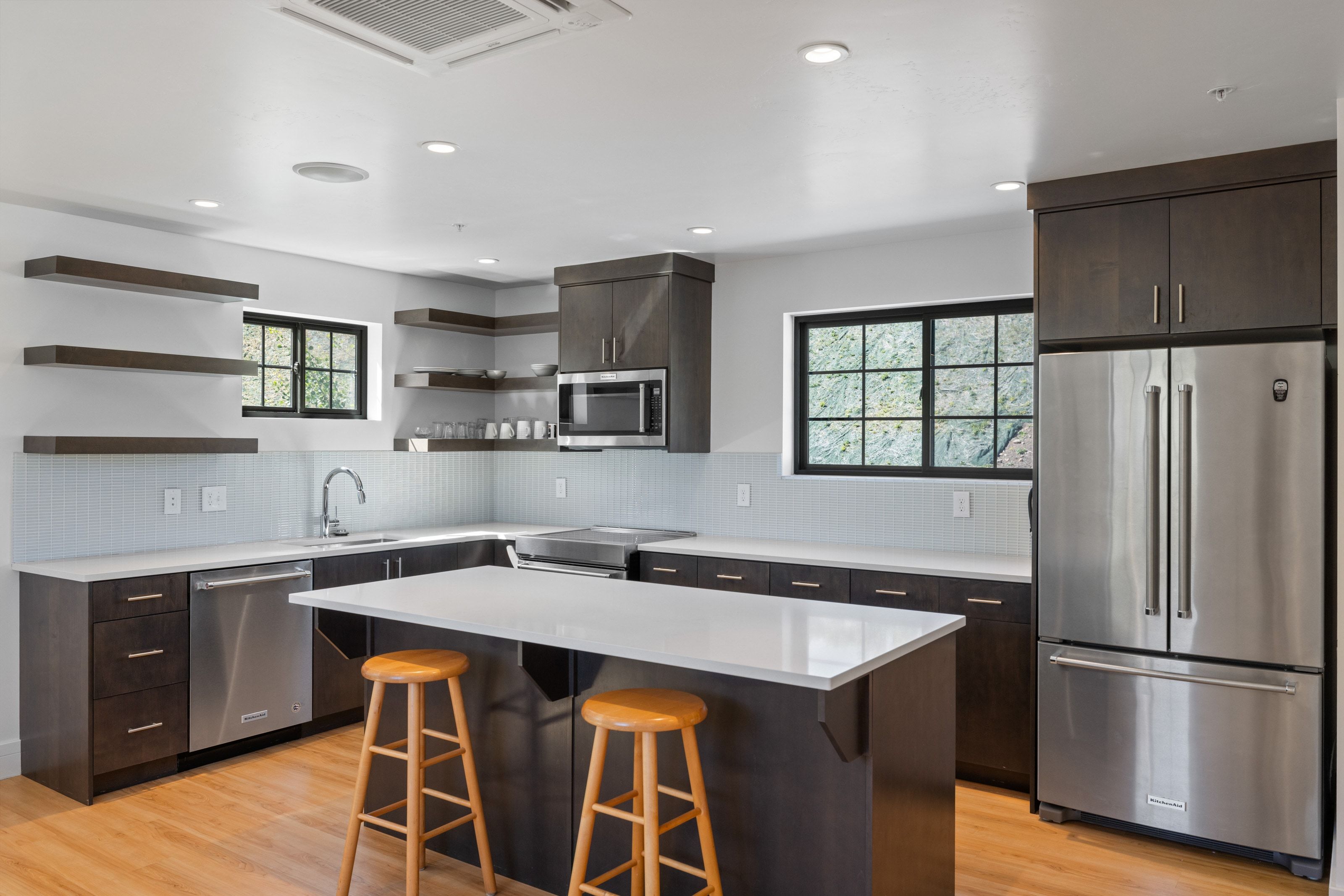 Modern kitchen featuring dark wood-finish cabinetry, stainless steel appliances, a center island with a light-toned countertop, wood-finish flooring, and recessed lighting