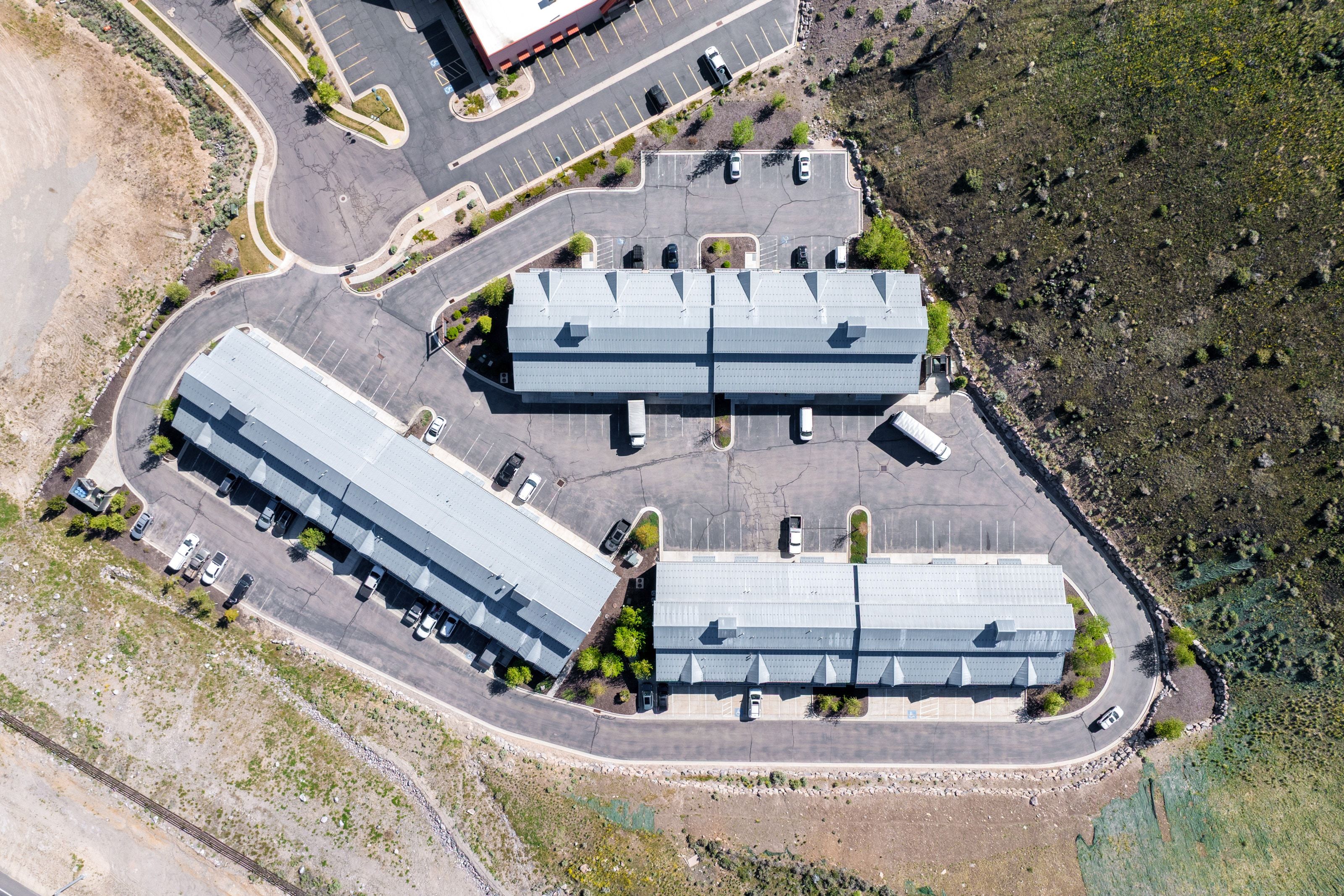 Aerial perspective showcasing multiple buildings with light-colored roofs, surrounded by extensive paved parking areas