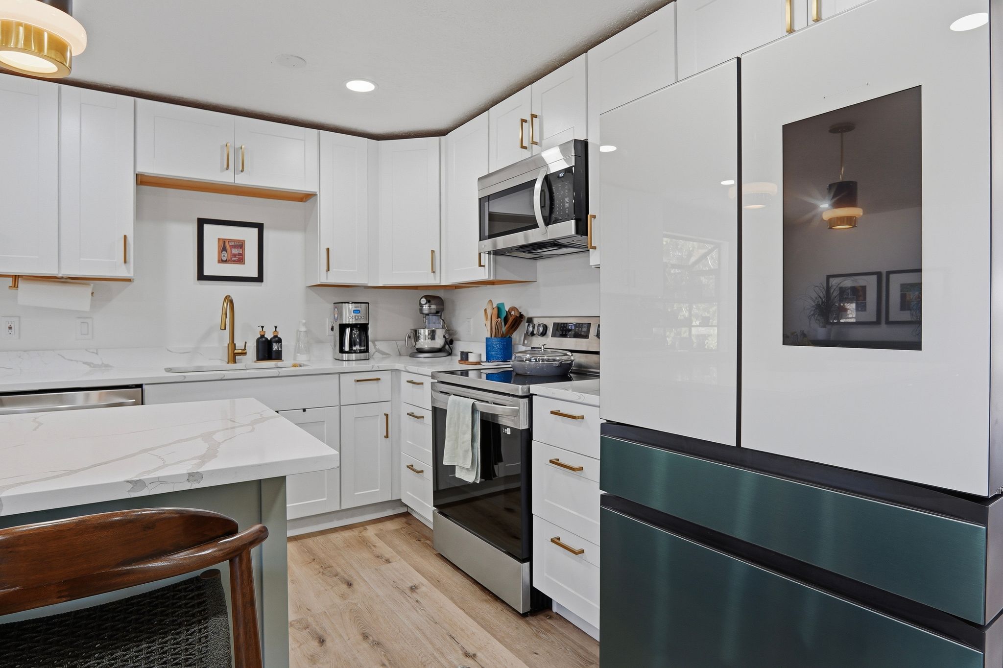 Modern kitchen featuring white cabinetry with gold-tone hardware, wood-finish flooring, stainless steel appliances, and light-toned countertops