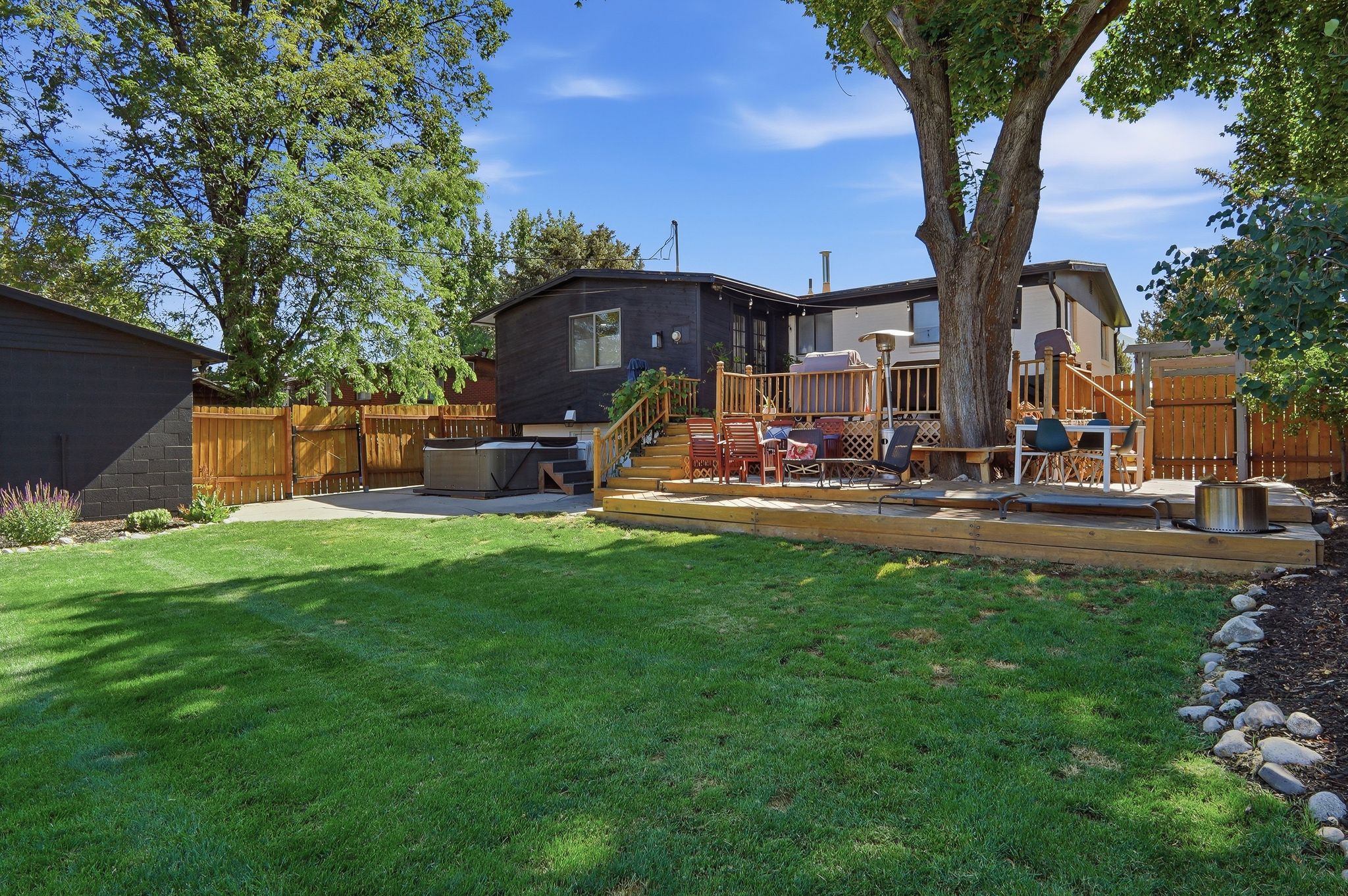 Expansive backyard featuring a manicured lawn, a multi-level wooden deck, and a hot tub
