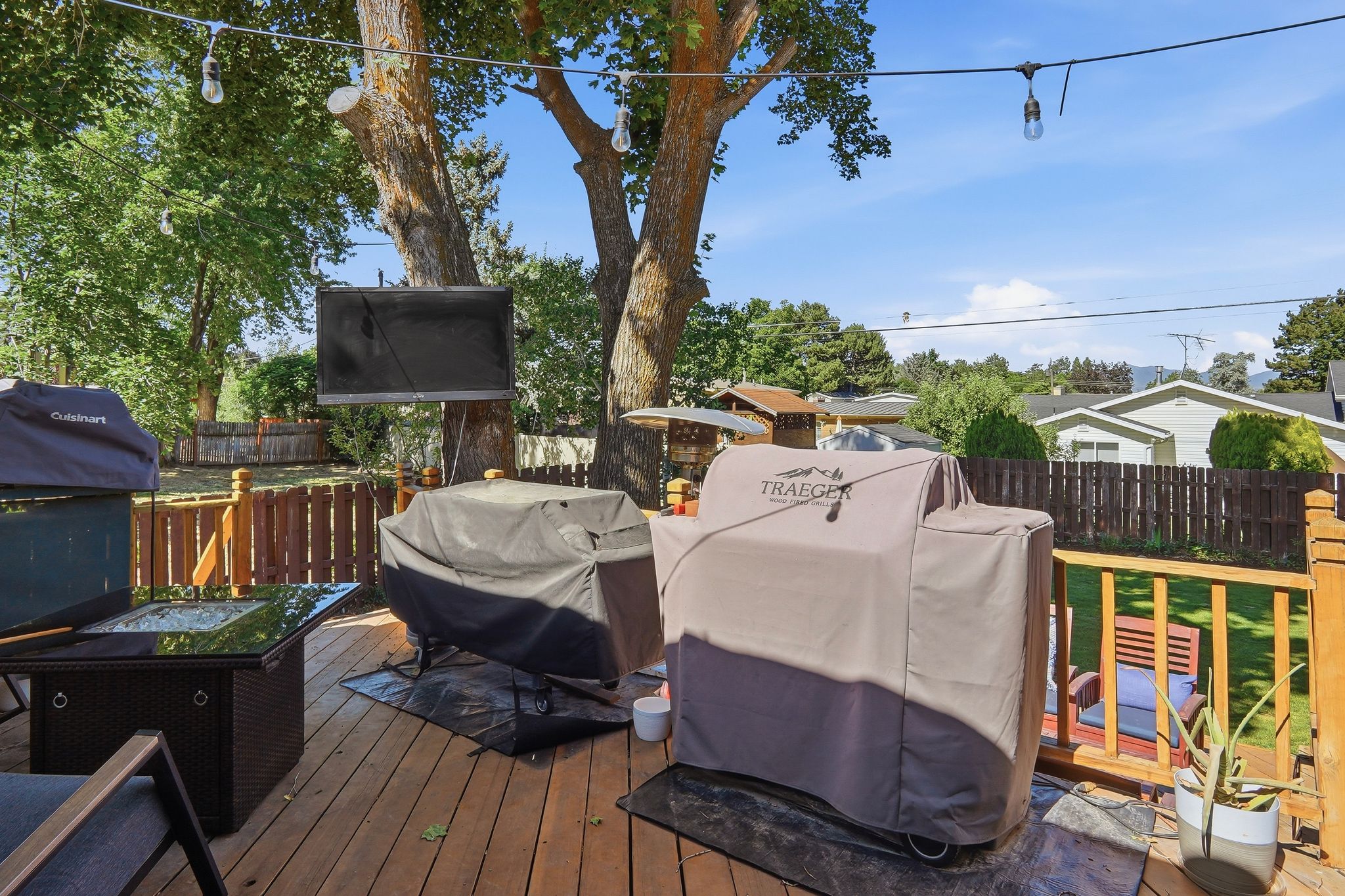 Wood-finish deck with a brown railing, string lighting, and mature trees overhead