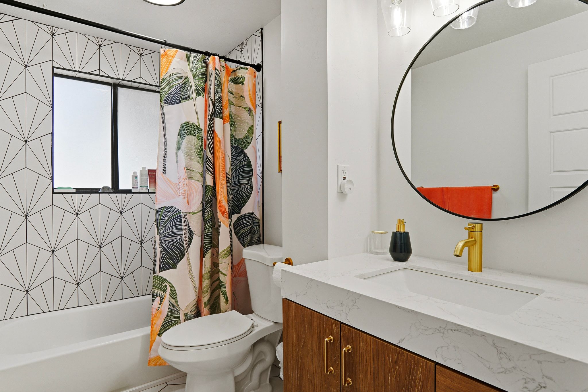 Bathroom featuring a white bathtub, geometric pattern wall tile, a window, a single vanity with wood-finish cabinetry, and a gold-tone faucet