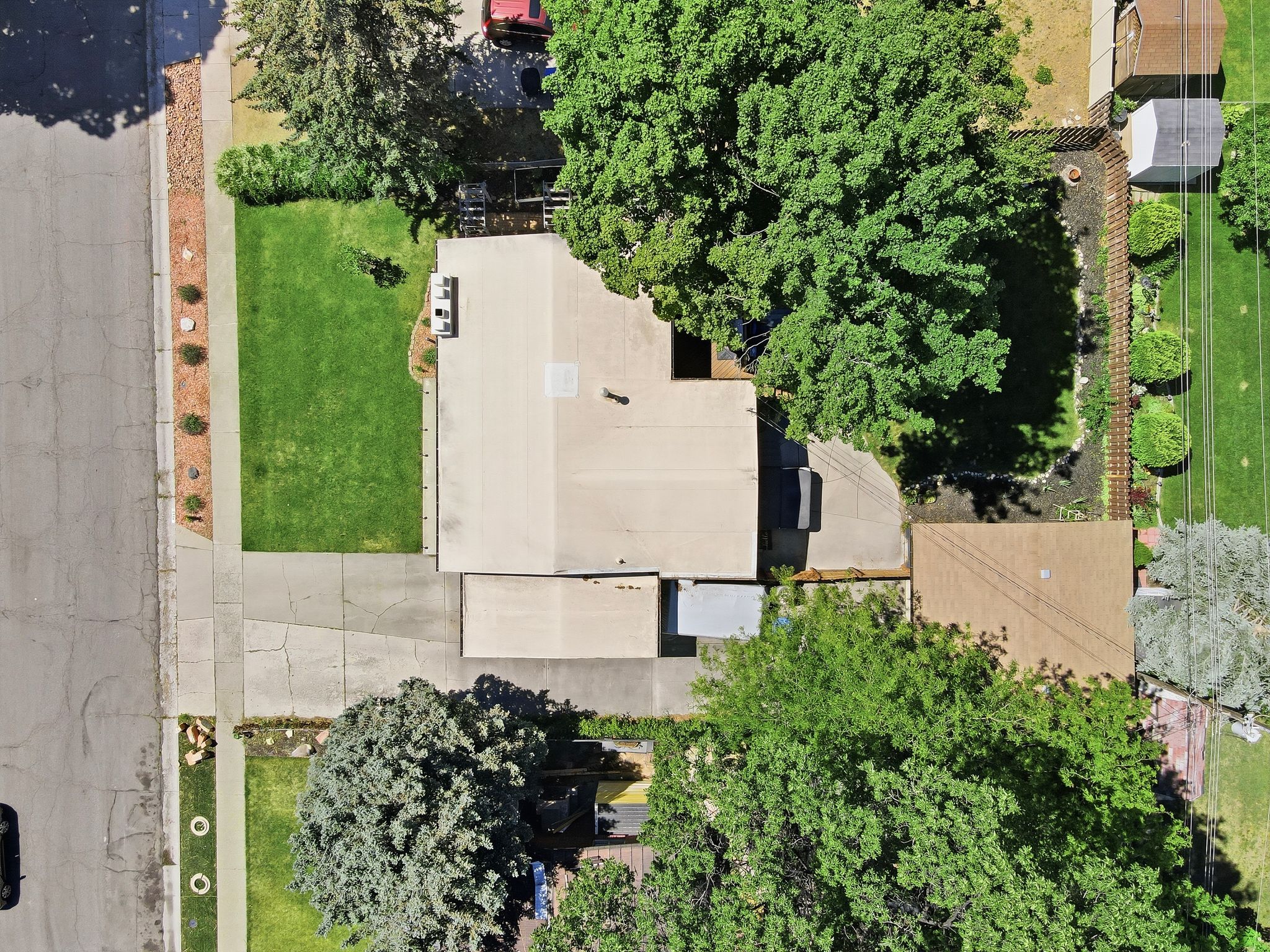 Property featuring a light-colored roof, mature trees, and a concrete driveway