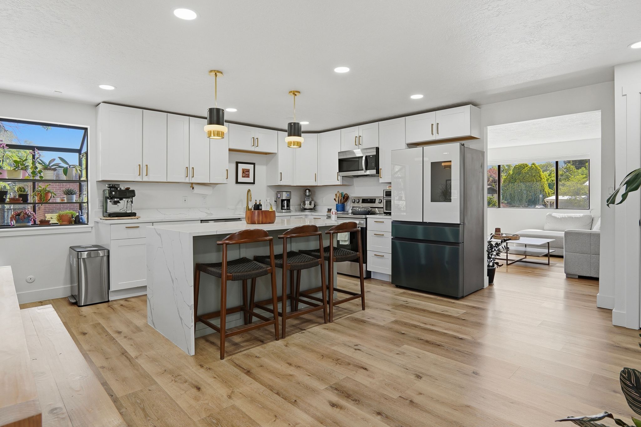 Kitchen featuring a waterfall island with stone countertop, white cabinetry with gold-tone hardware, wood-finish flooring, recessed lighting, and a large window