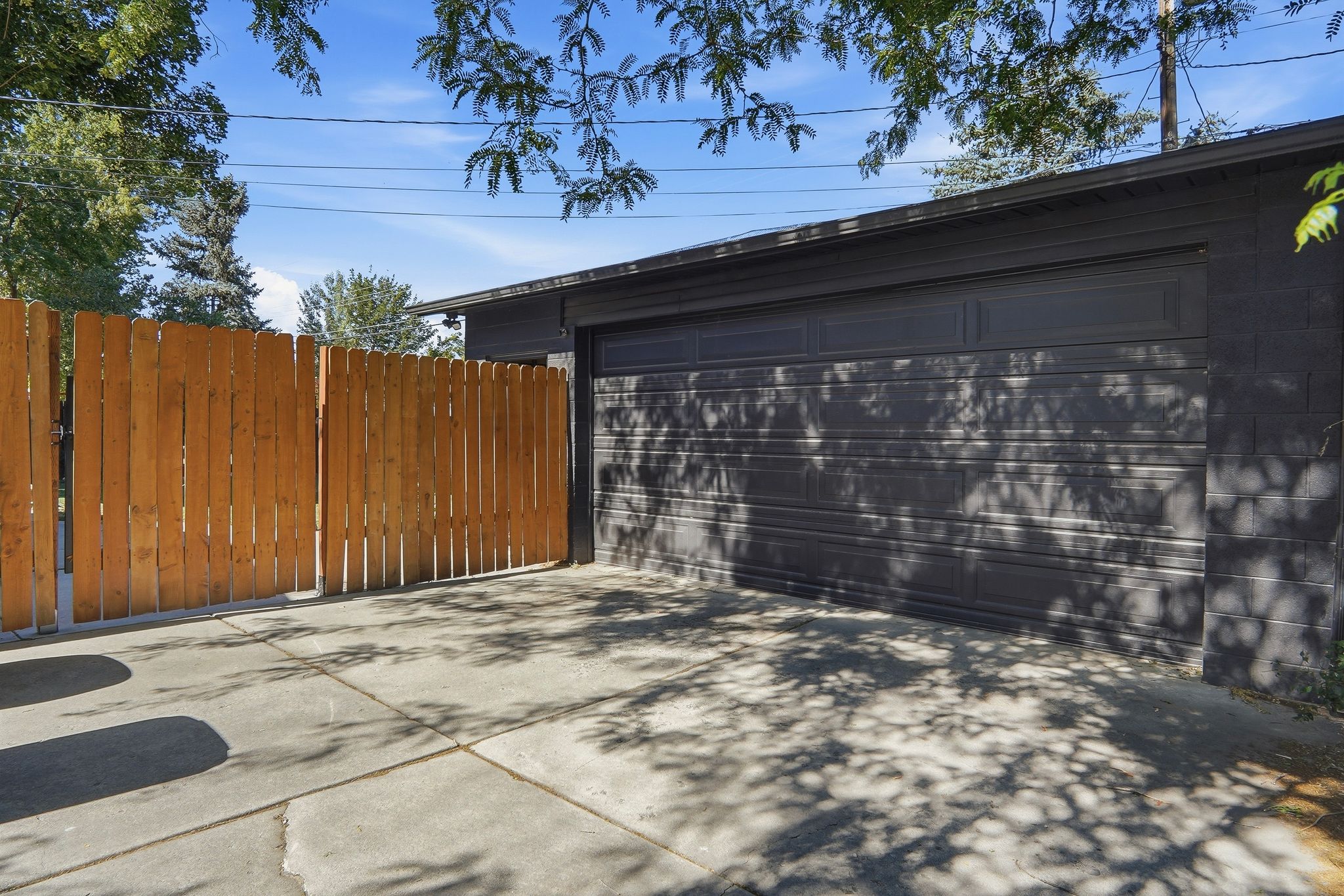 Detached garage with a dark panel door, concrete block siding, and a concrete driveway, complemented by a tall wooden privacy fence