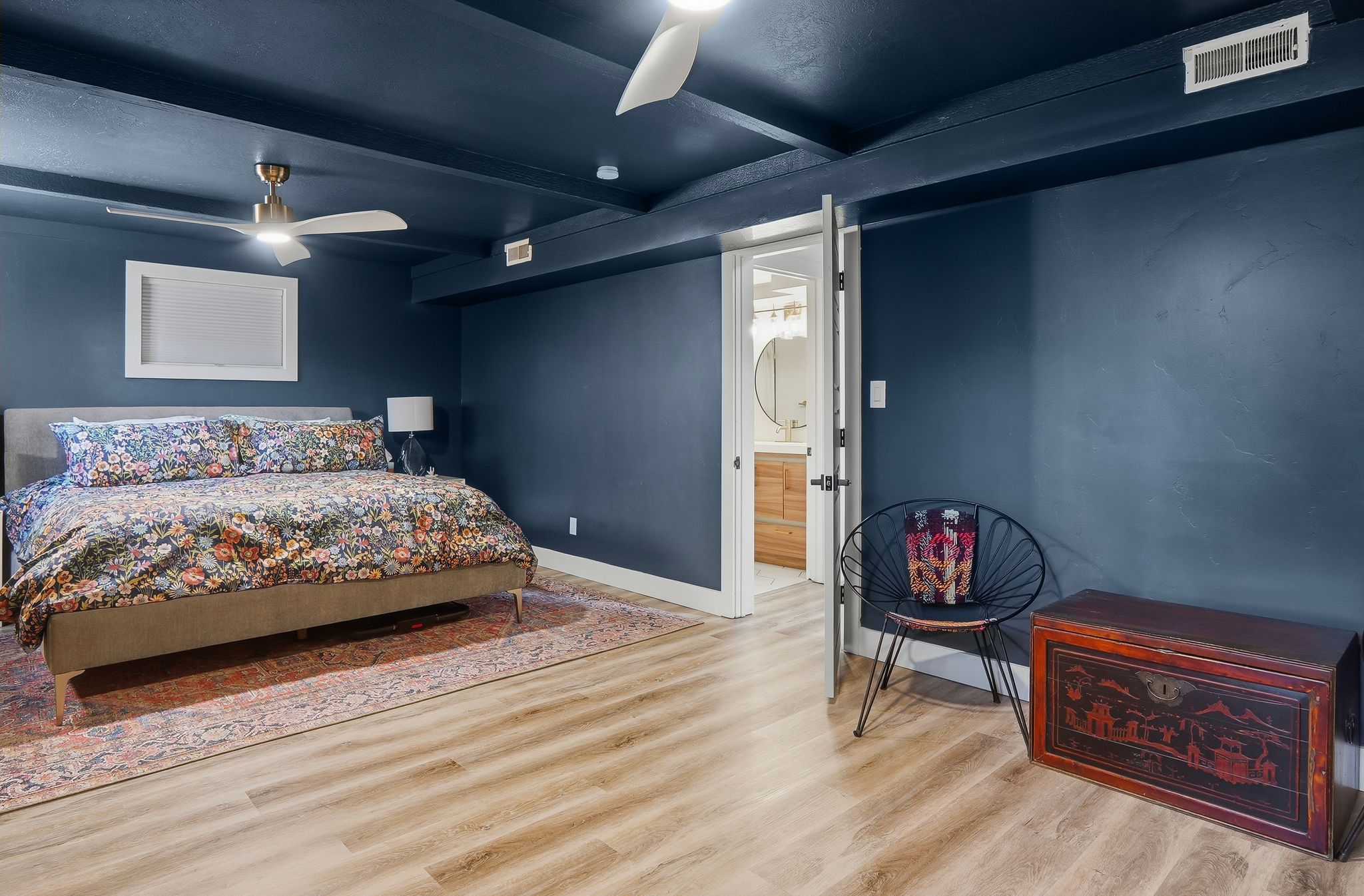 Bedroom featuring wood-finish flooring, dark accent walls, a ceiling fan with integrated lighting, recessed lighting, and a doorway leading to a bathroom with a vanity