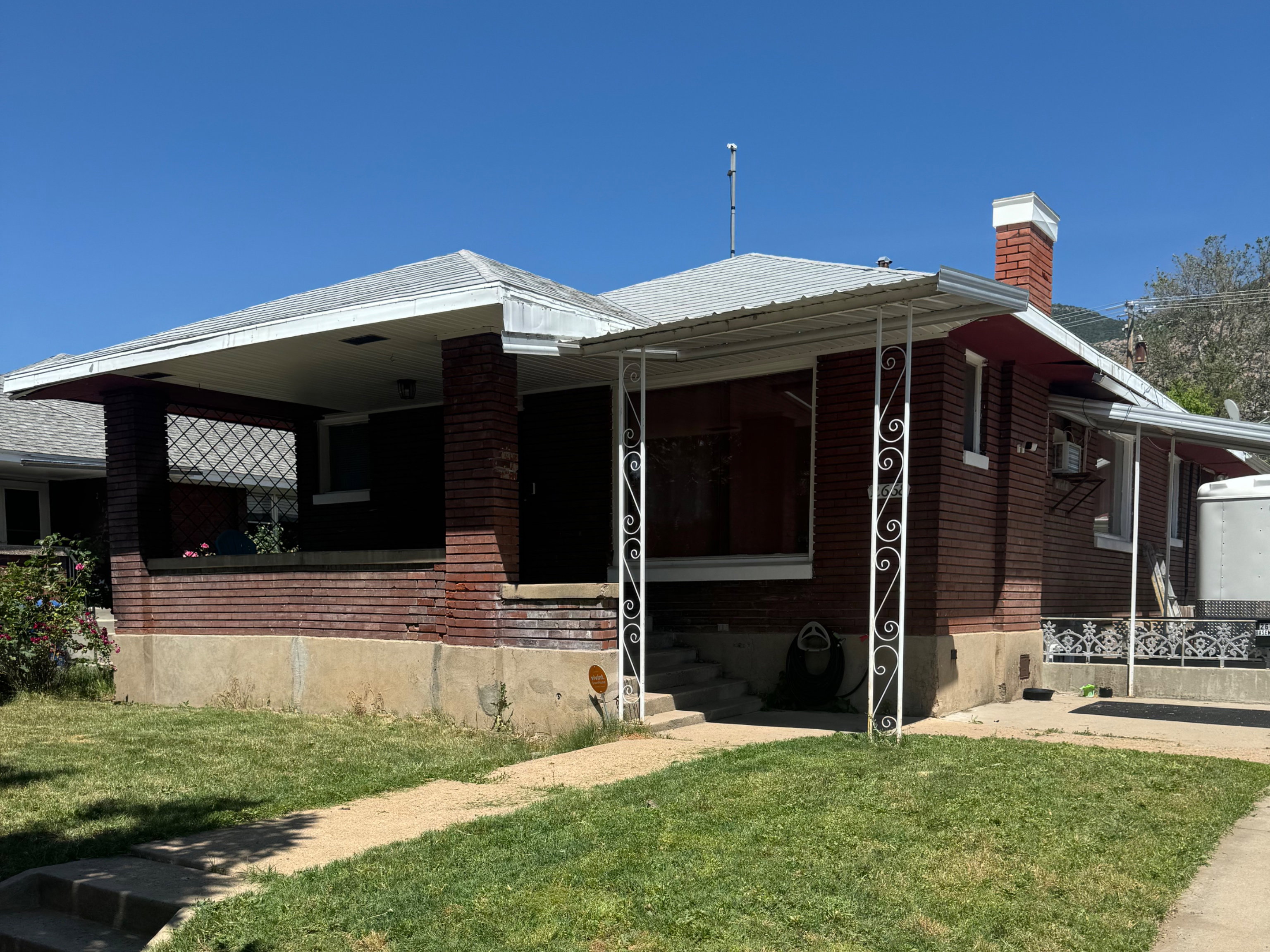 Brick exterior with a covered front porch featuring decorative metal supports, an additional side porch with similar metal accents, a brick chimney, and a concrete walkway