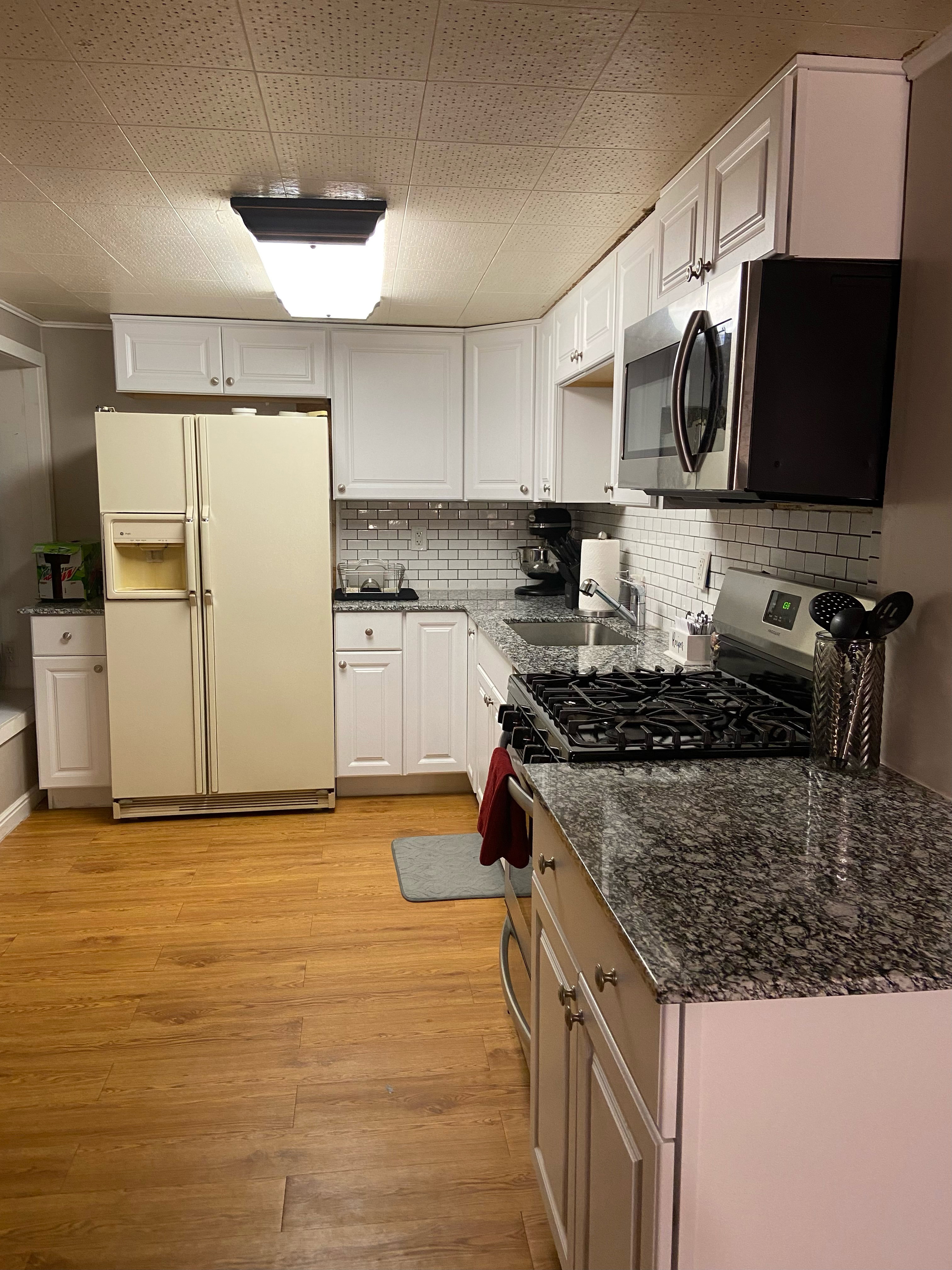 Kitchen featuring white cabinetry, granite countertops, subway tile backsplash, wood-finish flooring, and stainless steel appliances