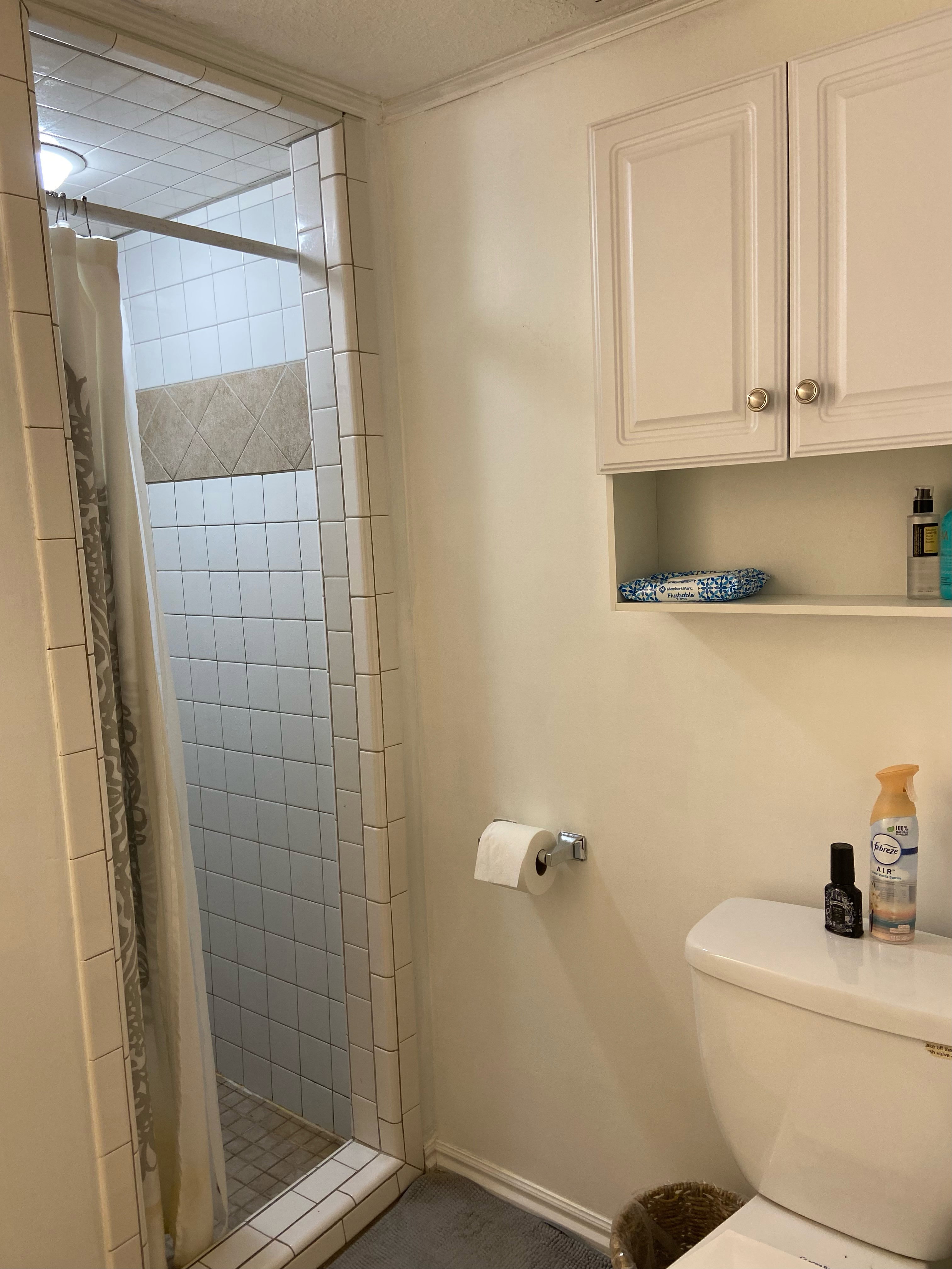 Tiled shower enclosure with a horizontal accent band, accompanied by white cabinetry featuring integrated shelving