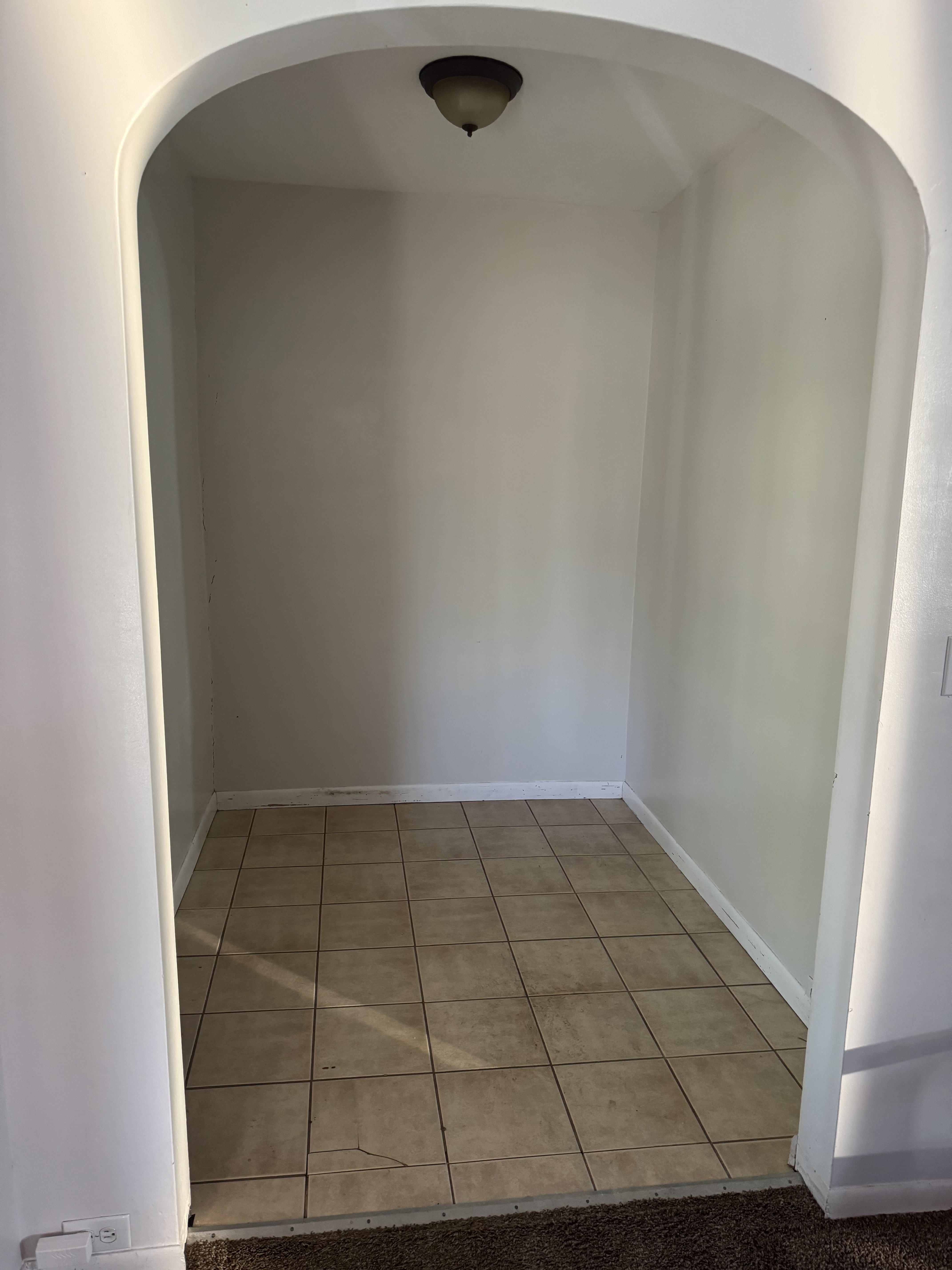 Arched entryway leading to an alcove with square tile flooring, baseboard trim, and a ceiling-mounted light fixture