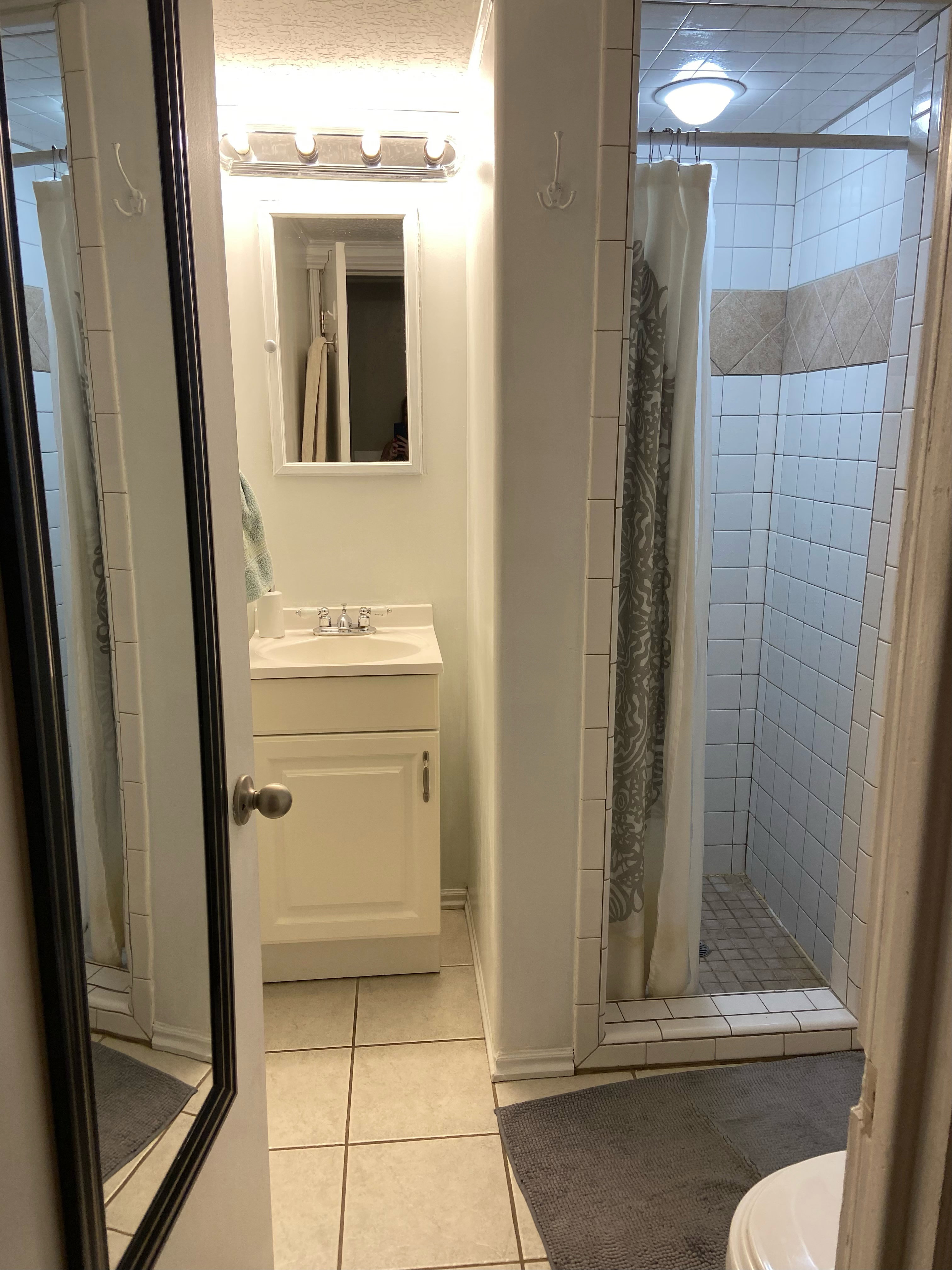 Bathroom featuring a single vanity with storage cabinet, rectangular mirror, and a three-light fixture