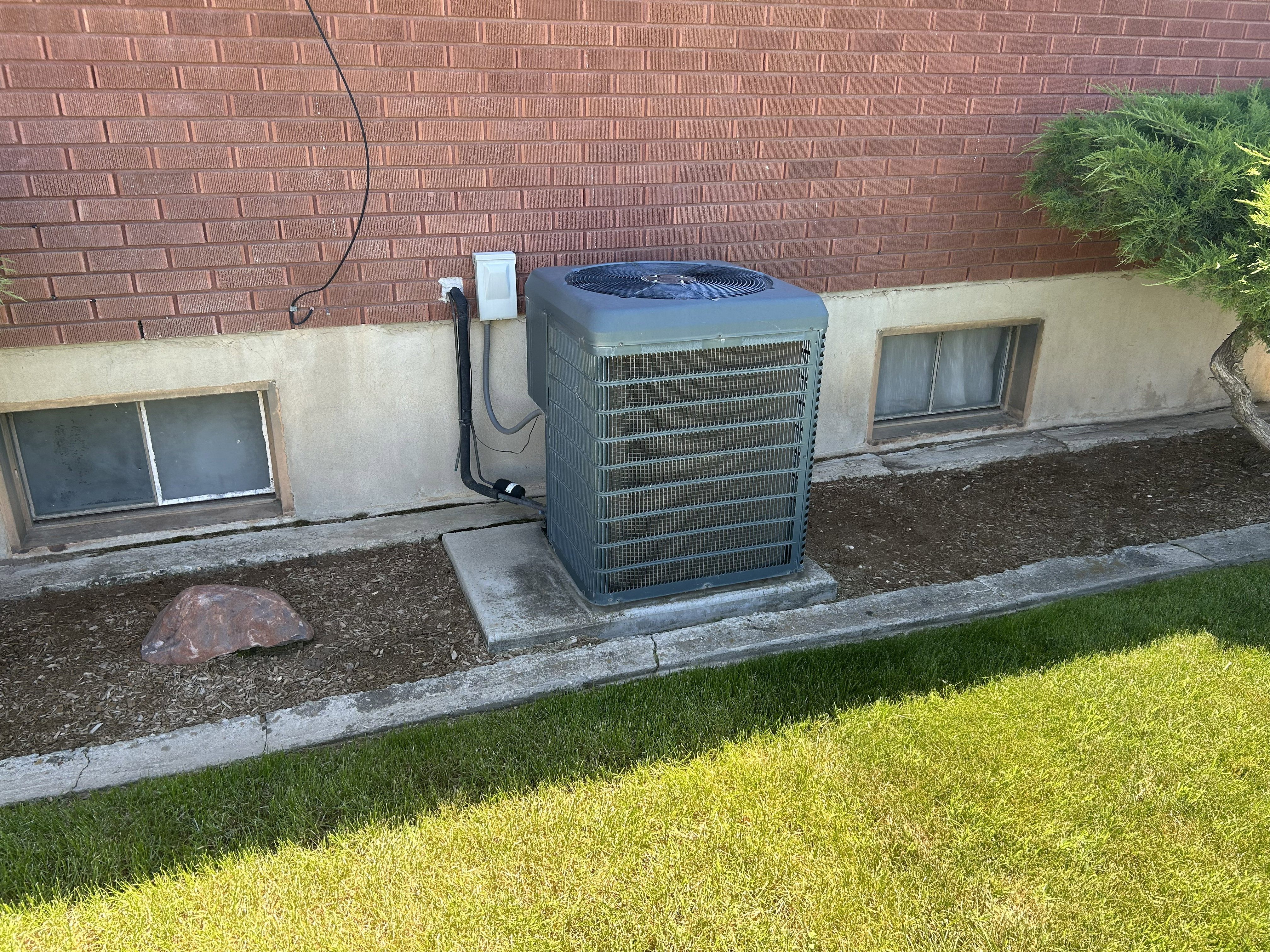 Brick veneer exterior with a foundational stucco band, featuring a central HVAC unit on a concrete pad