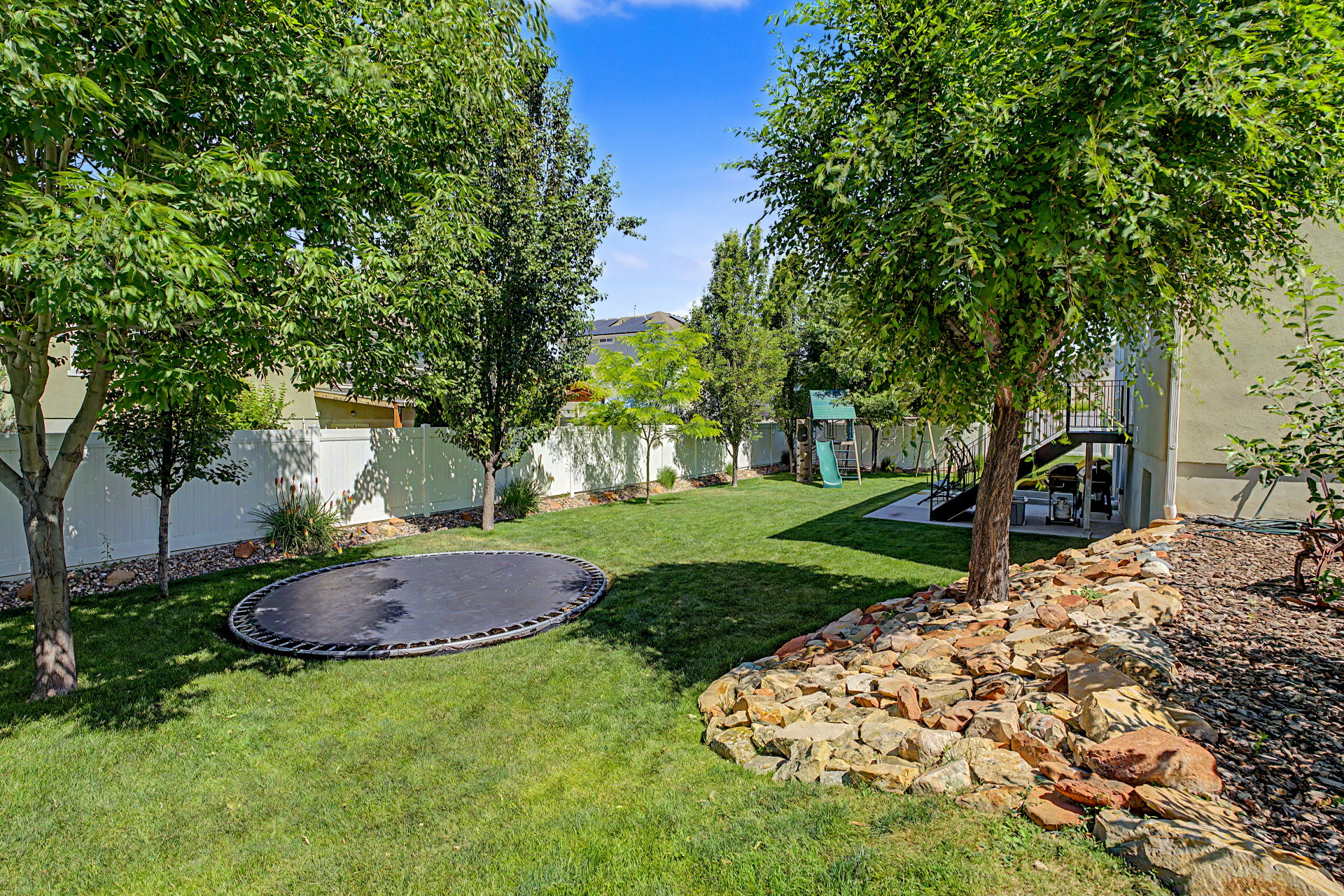 Expansive green lawn with mature trees and a white privacy fence