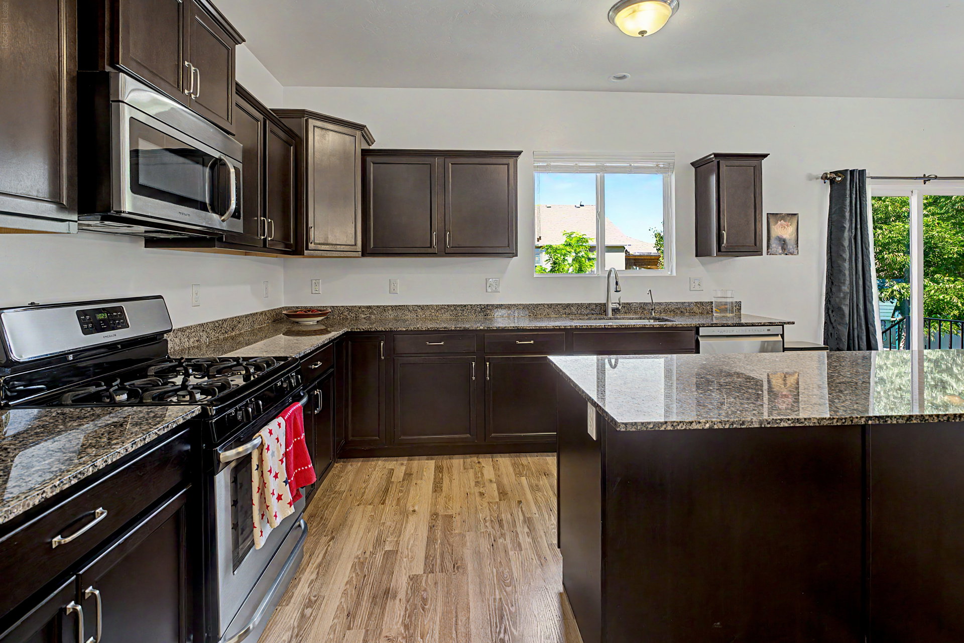 Kitchen featuring dark wood cabinetry, granite countertops, stainless steel appliances, wood-finish flooring, and a central island