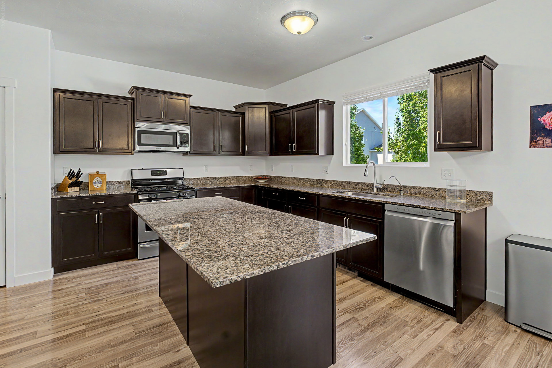 Kitchen featuring dark wood cabinetry, granite countertops, wood-finish flooring, a stainless steel gas range, and a stainless steel dishwasher
