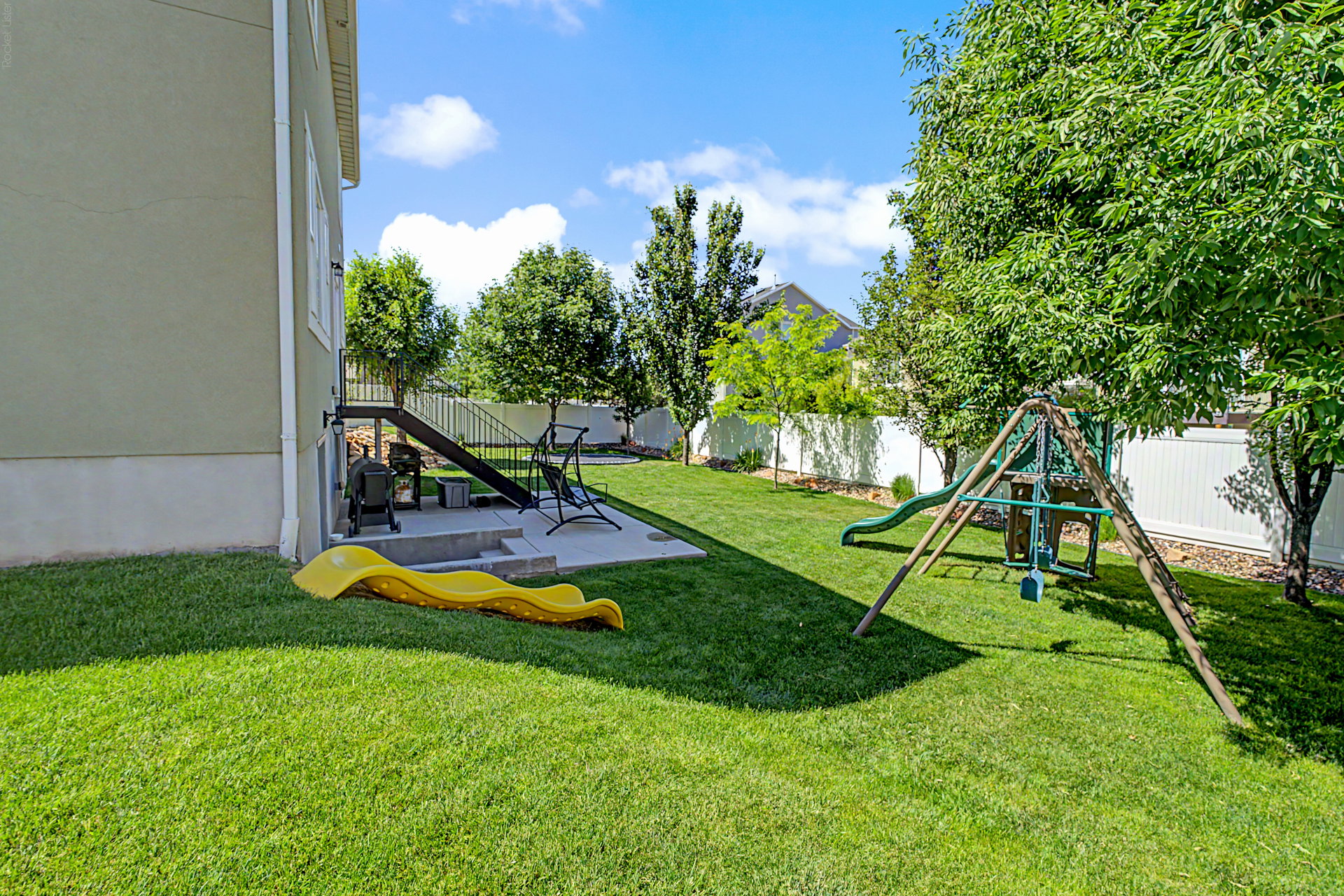 Expansive backyard featuring a manicured lawn, established shade trees, and a white privacy fence