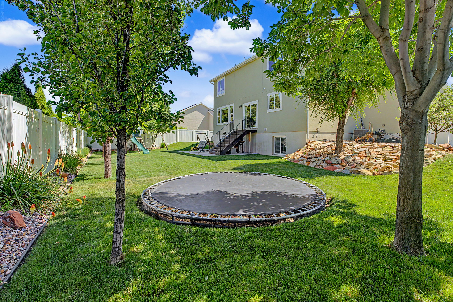 Expansive green lawn backyard featuring mature trees, a privacy fence, and a stone retaining wall