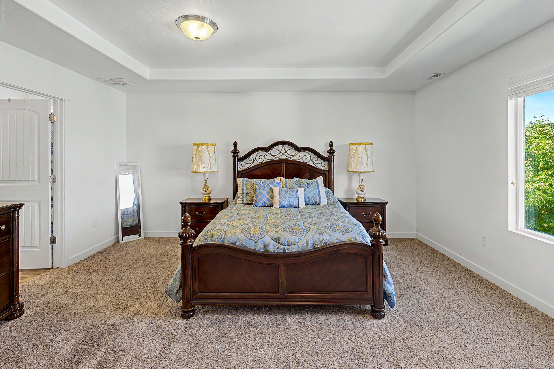 Tray ceiling featuring an overhead light fixture, light-toned carpeting, white walls, and a window with outdoor scenery