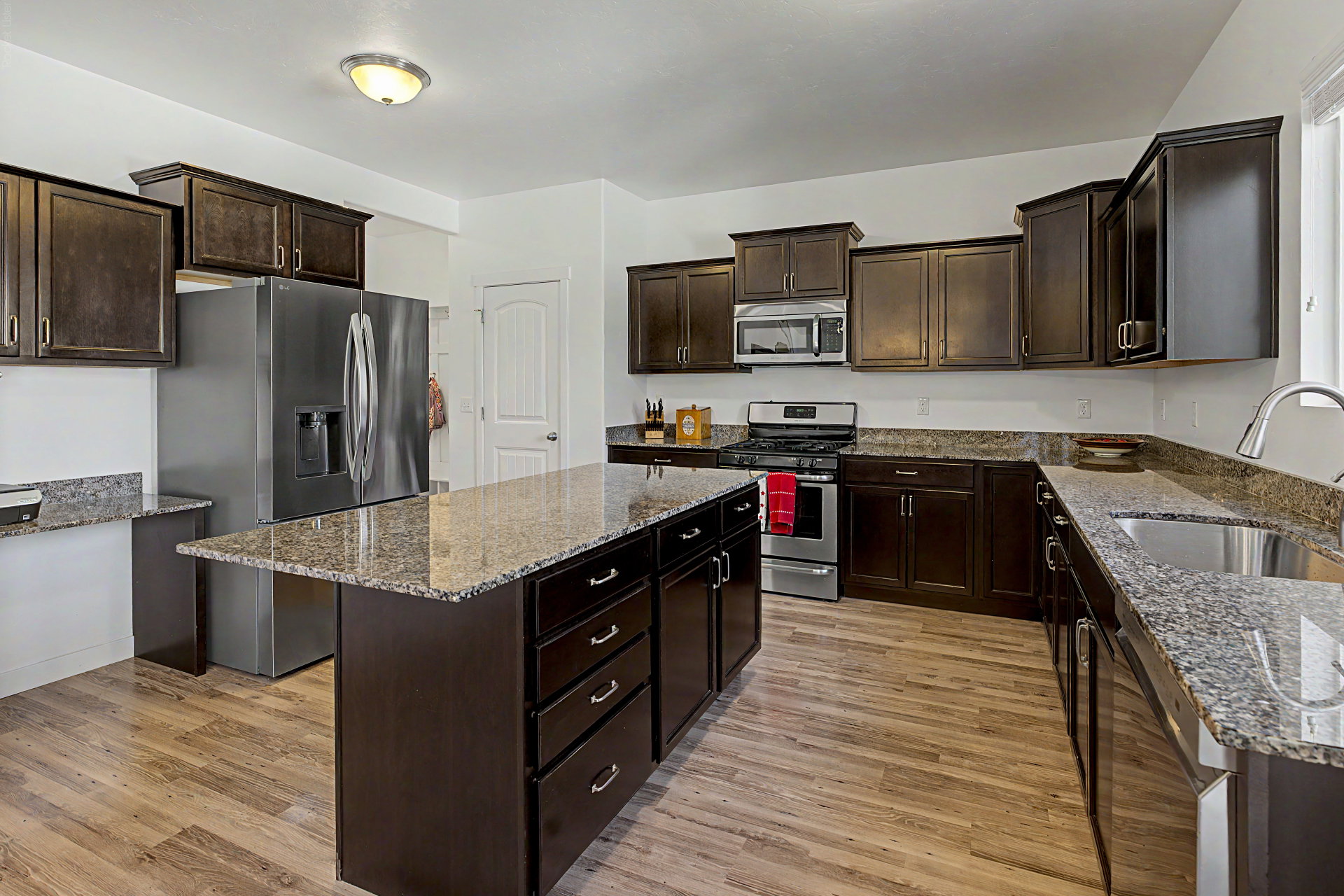 Kitchen featuring a central island, wood-finish flooring, dark wood cabinetry, and granite countertops