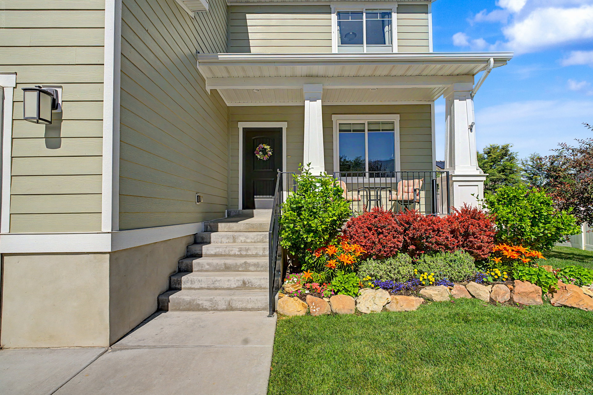 Welcoming covered porch with decorative railing, concrete steps, and established landscaping