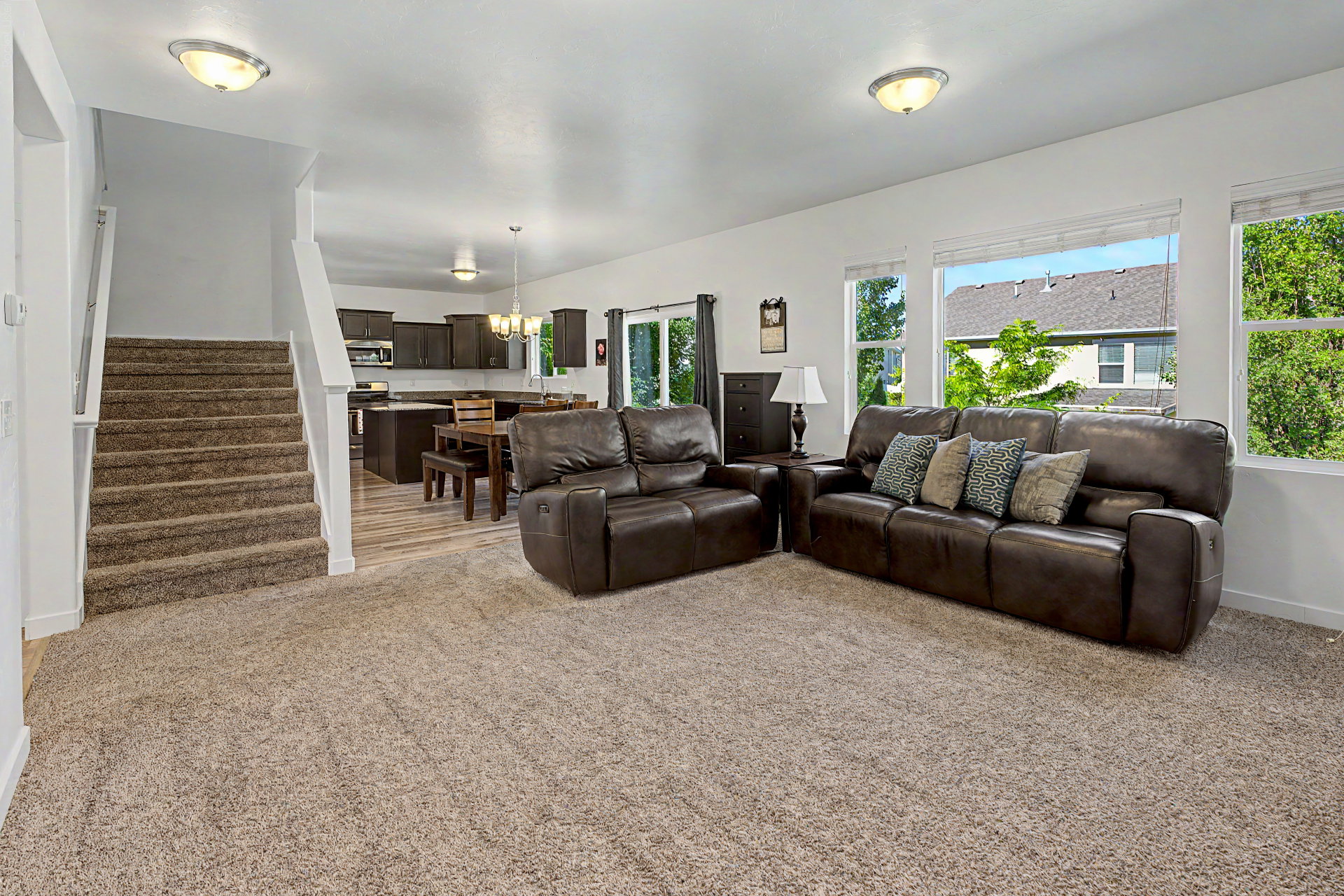 Open-concept living space featuring carpeted flooring and an adjacent staircase