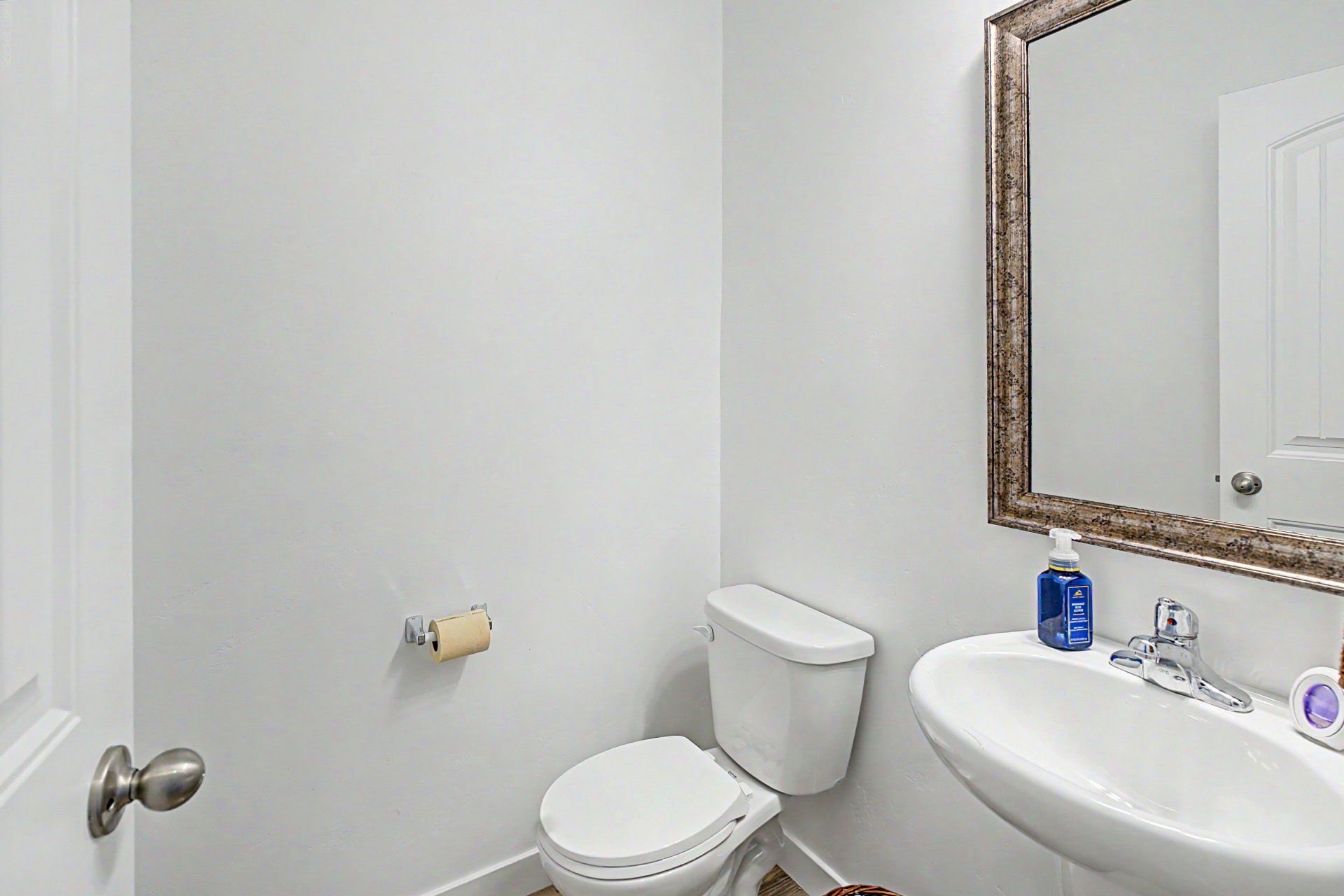 Bathroom featuring a white toilet, pedestal sink, and a decorative framed mirror