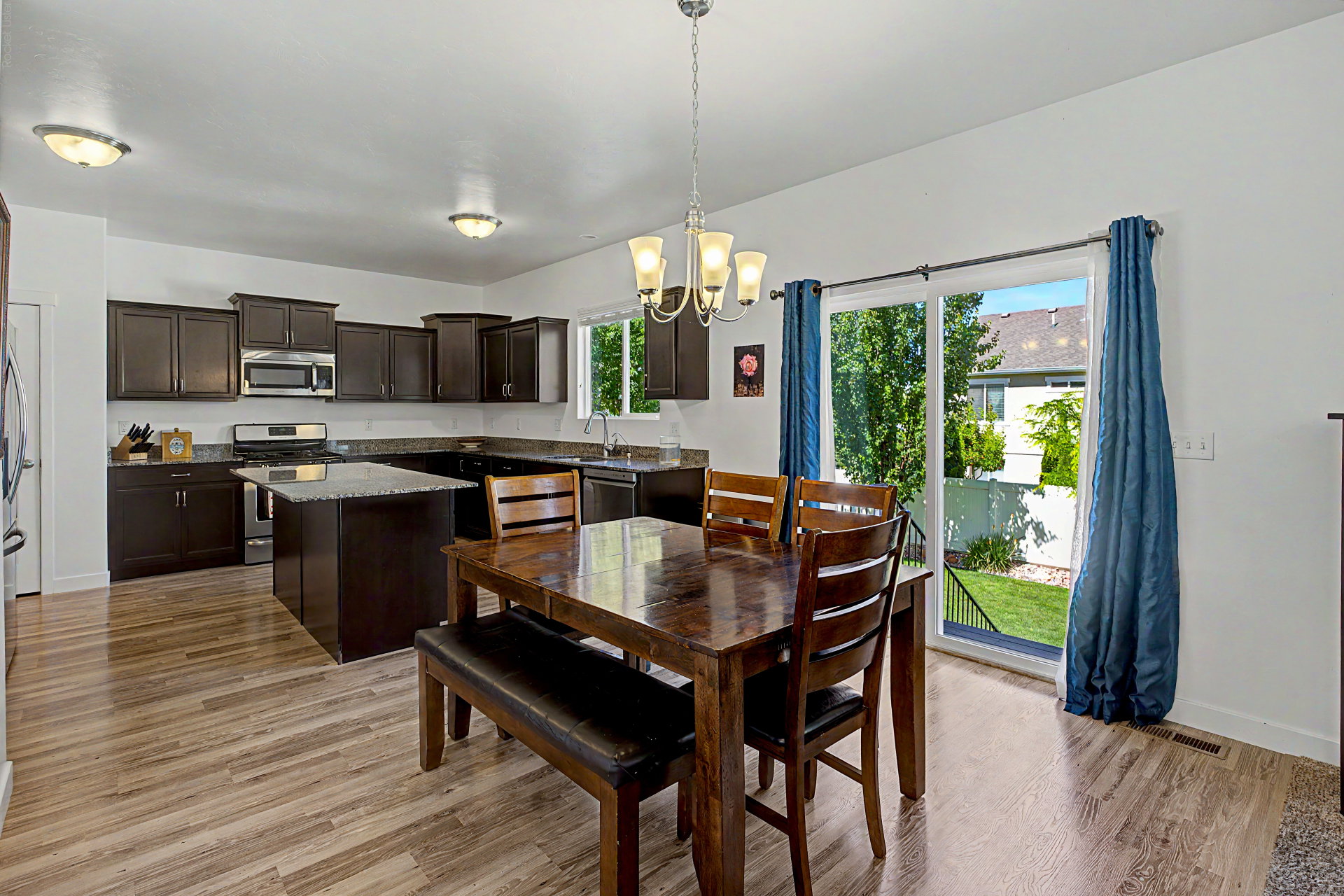 Open-concept kitchen and dining area featuring dark wood-finish cabinetry, stainless steel appliances, and a central kitchen island with a stone countertop