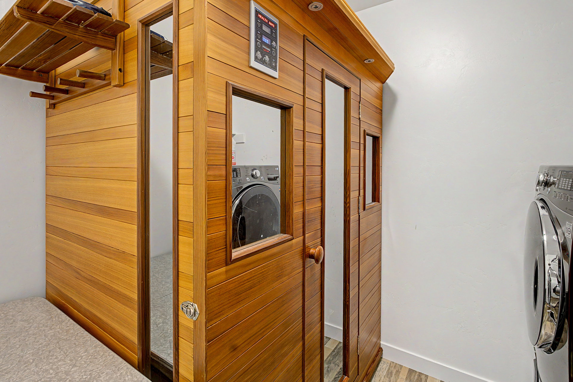 Integrated wood-paneled sauna featuring a glass door, window, and wall-mounted controls