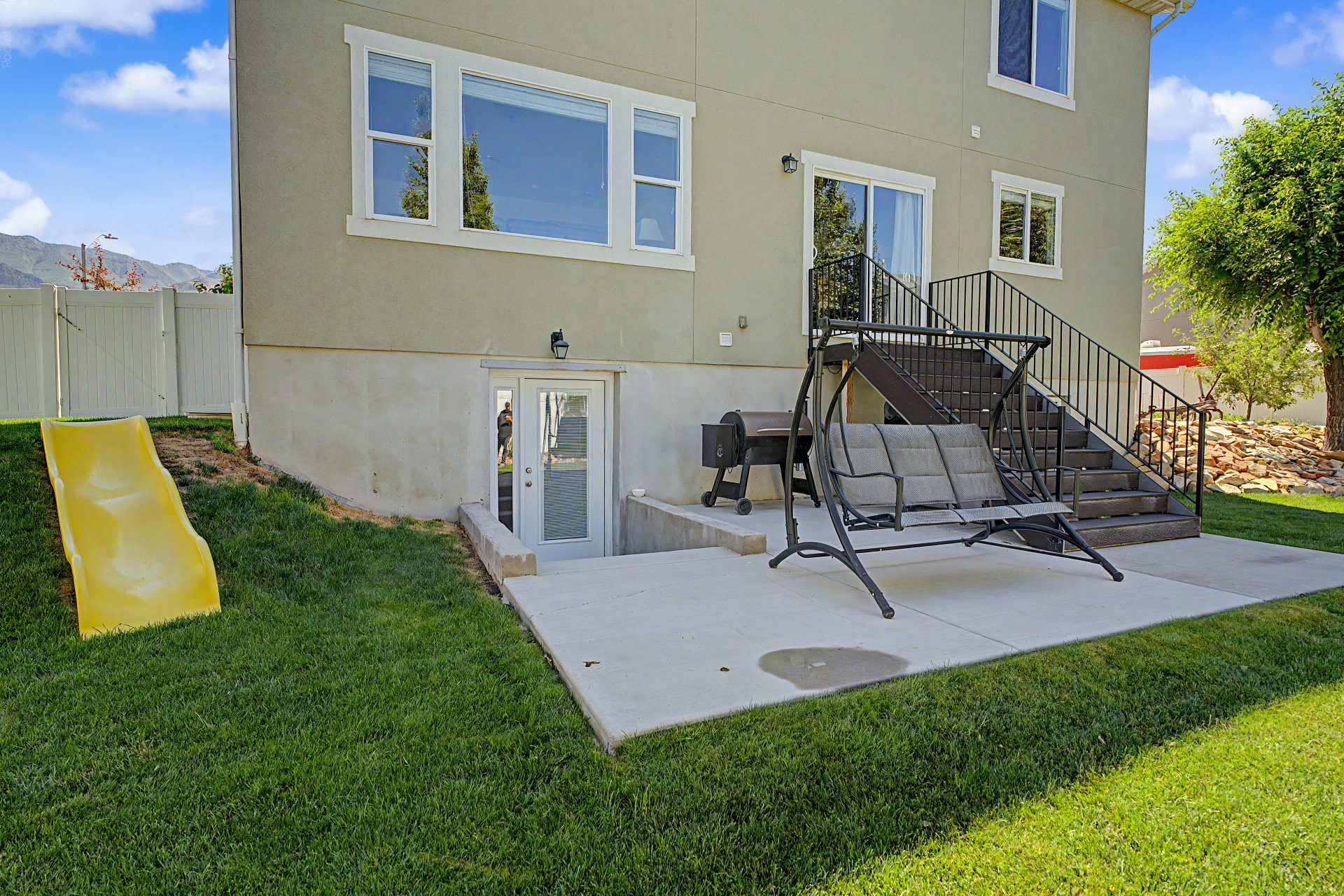 Rear exterior featuring a concrete patio, exterior staircase with metal railings, and a walk-out basement door with glass paneling