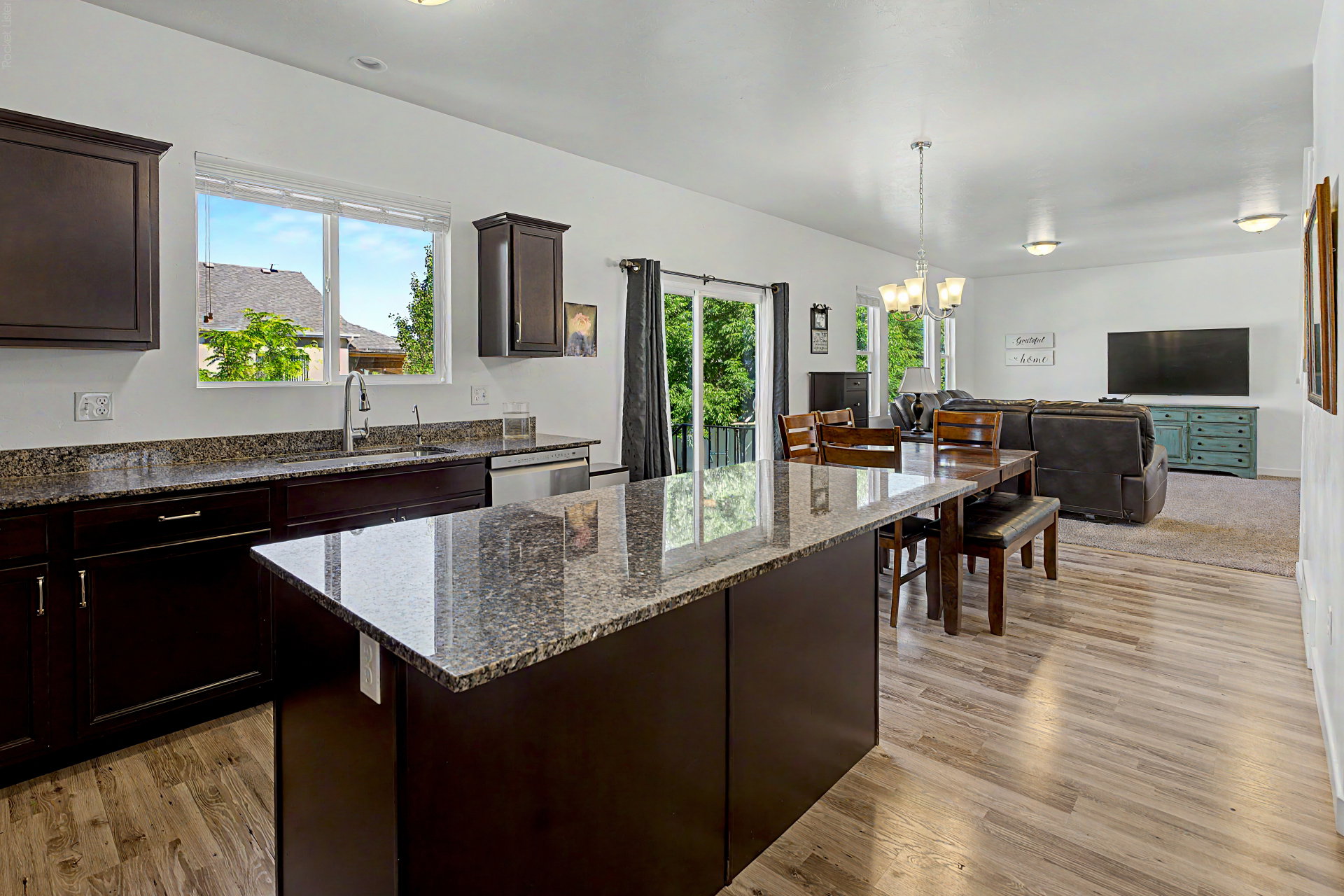 Open-concept kitchen featuring dark wood cabinetry, granite countertops, an island with seating, stainless steel appliances, and wood-finish flooring