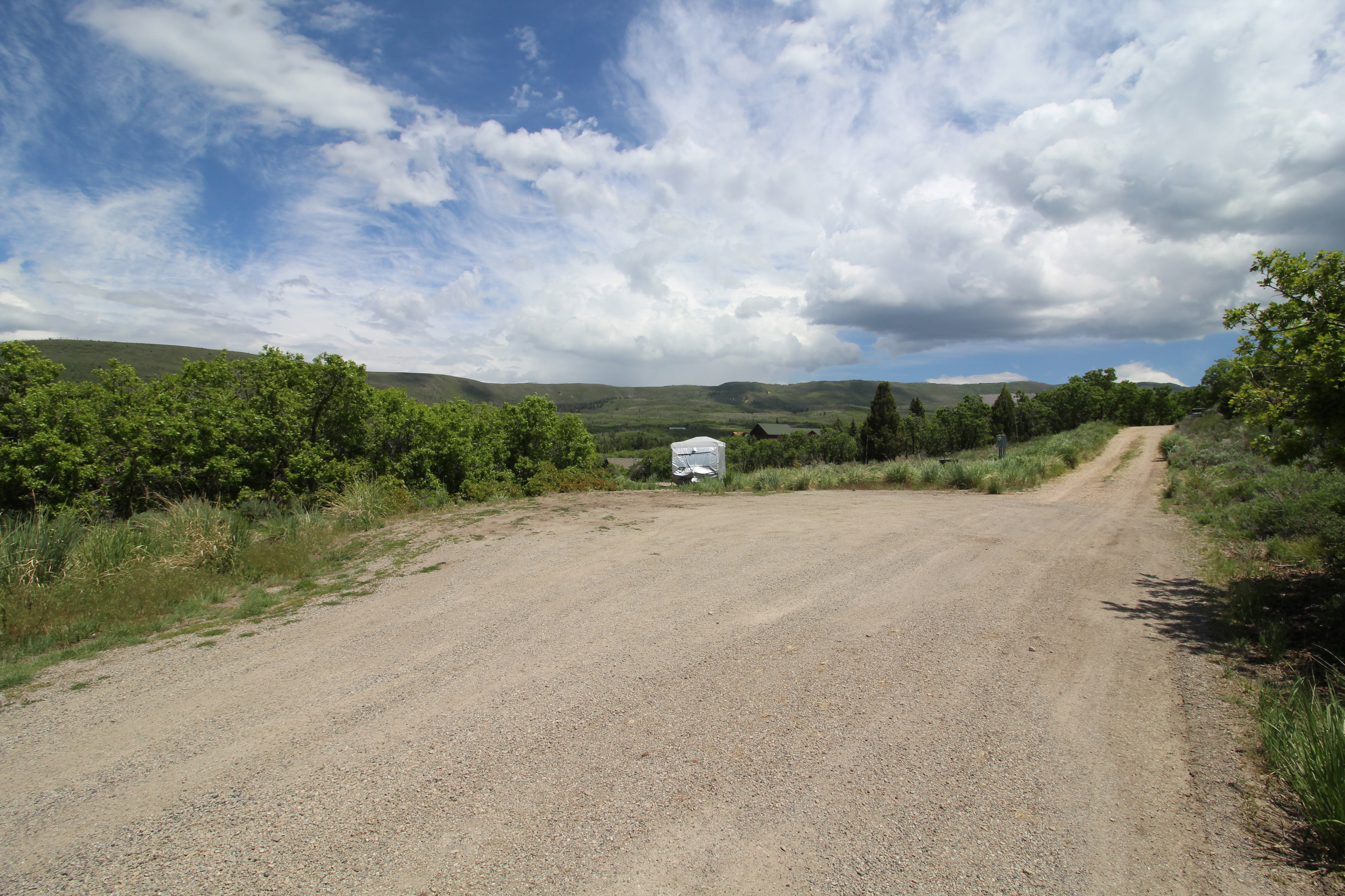 Gravel road entrance with surrounding natural vegetation and distant rolling hills