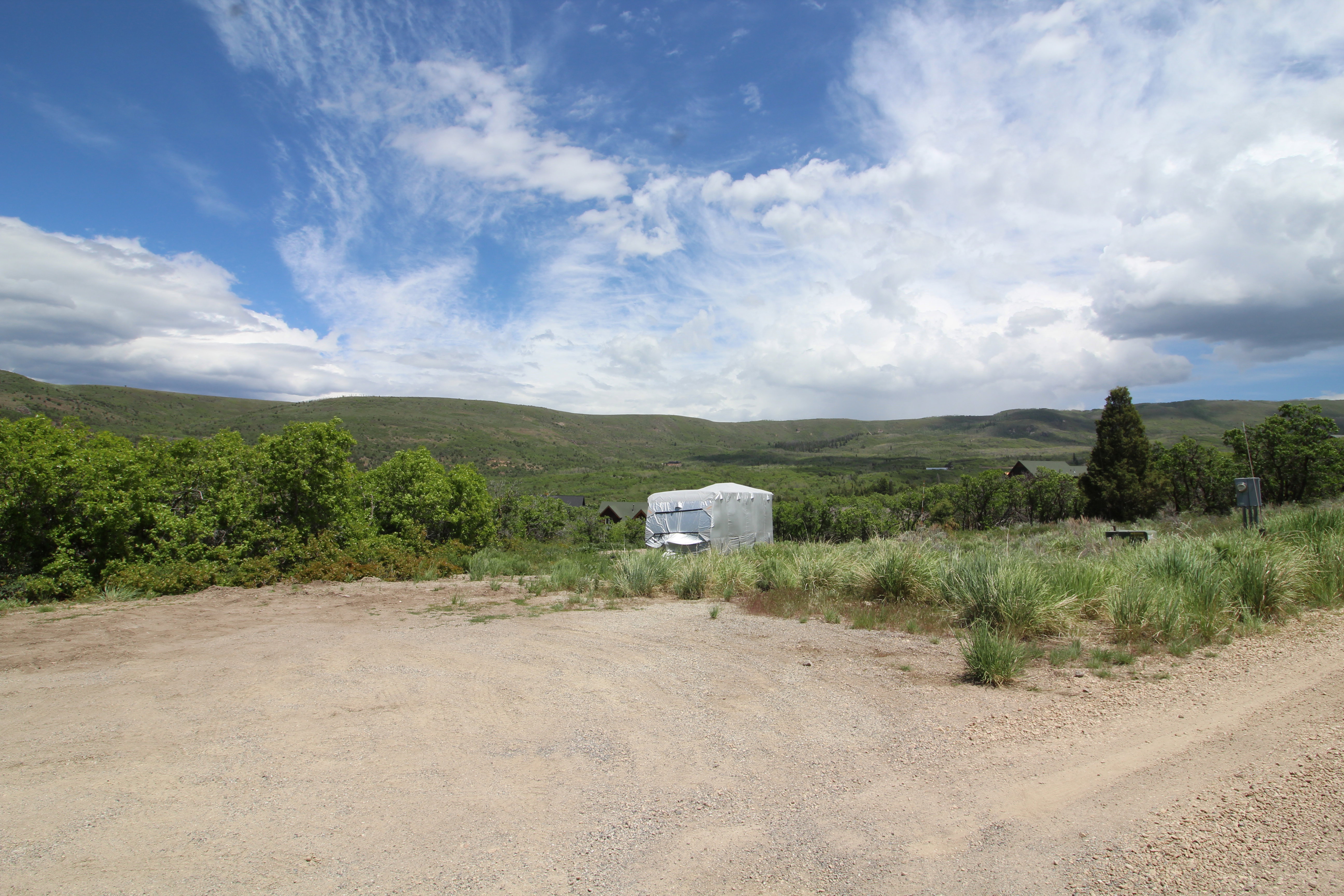 Expansive undeveloped lot featuring a natural terrain, distant mountainous backdrop, mature trees, and broad skies