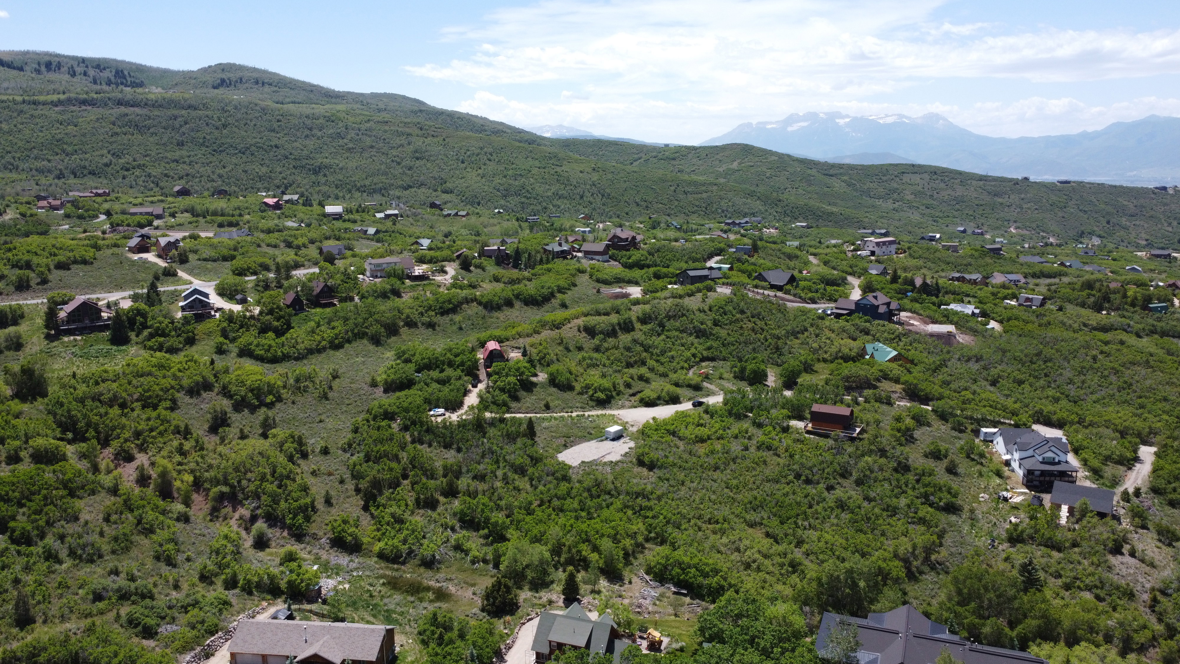 Expansive mountainous terrain featuring scattered residential properties, verdant foliage, and distant snow-capped peaks