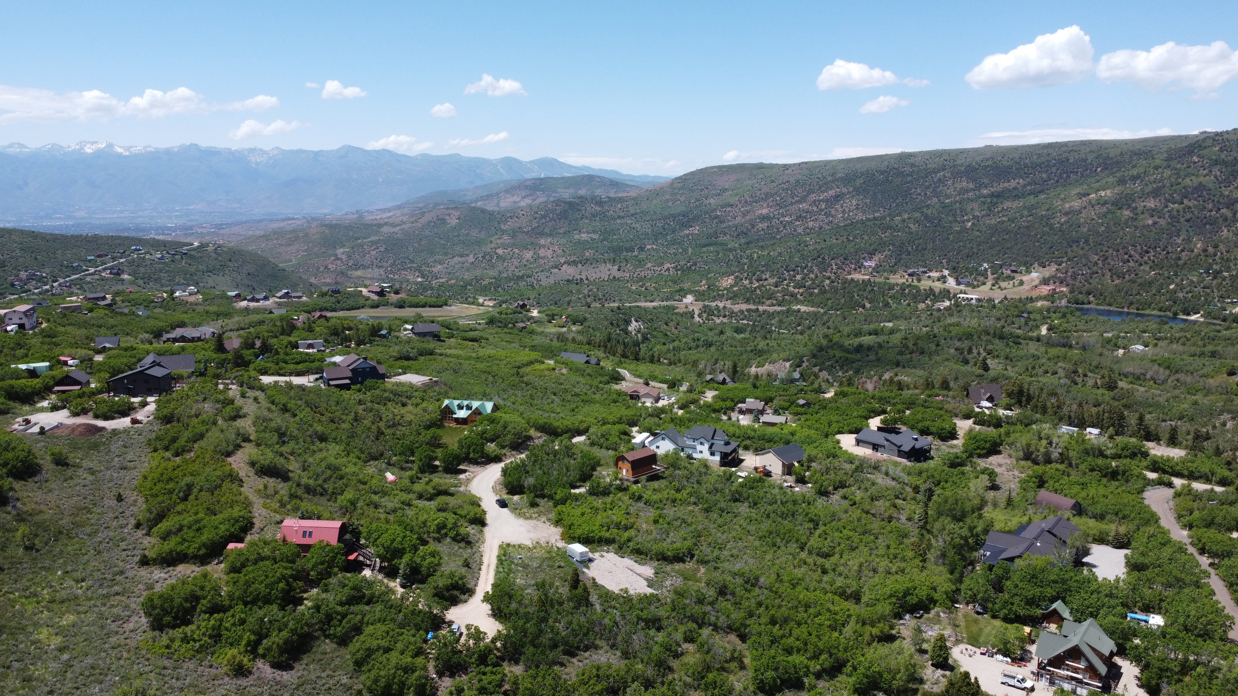 Expansive mountain landscape featuring numerous properties nestled within abundant greenery and distant snow-capped peaks
