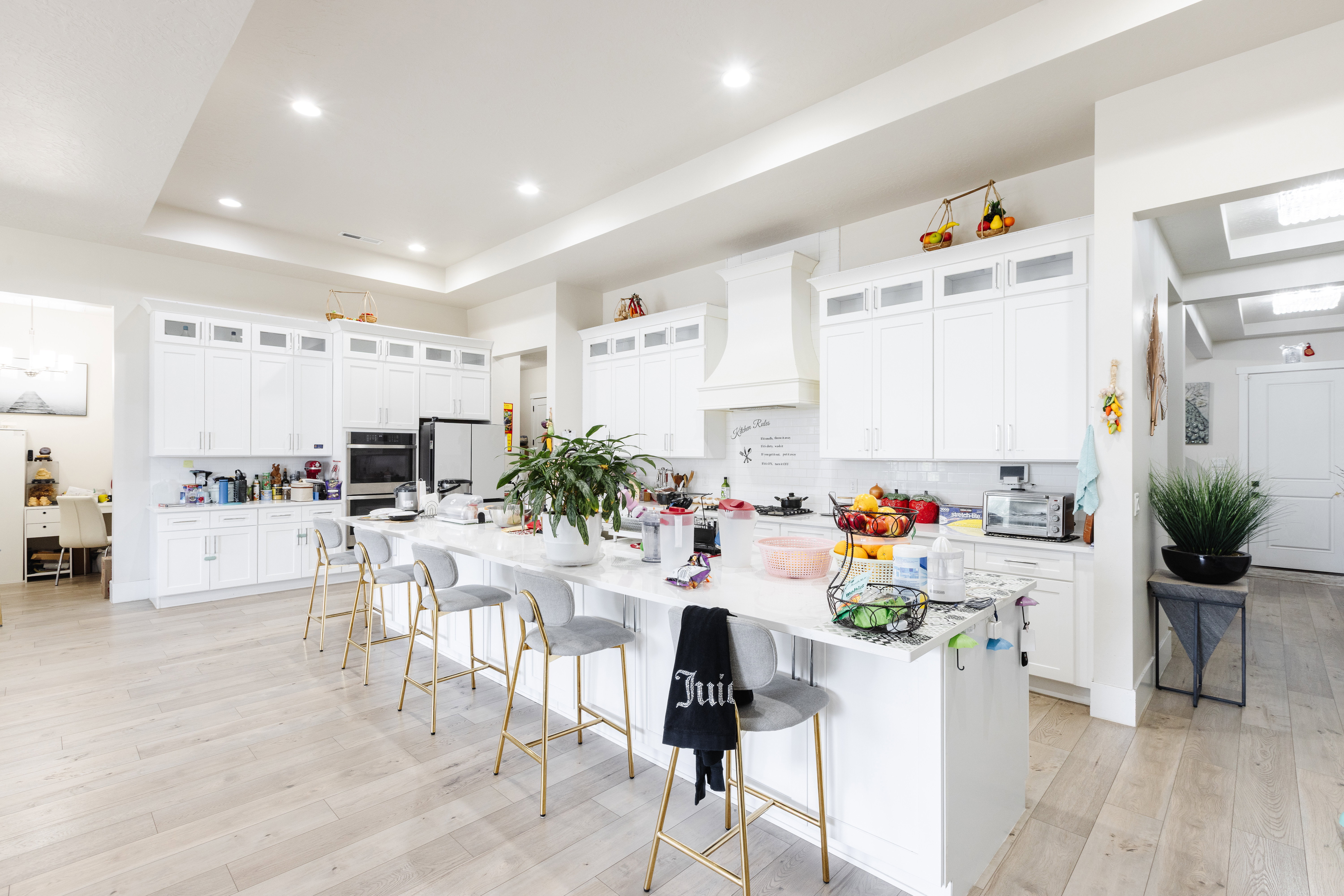 Spacious kitchen featuring an oversized island with counter seating, extensive white cabinetry, light wood-finish flooring, recessed lighting, and a built-in oven
