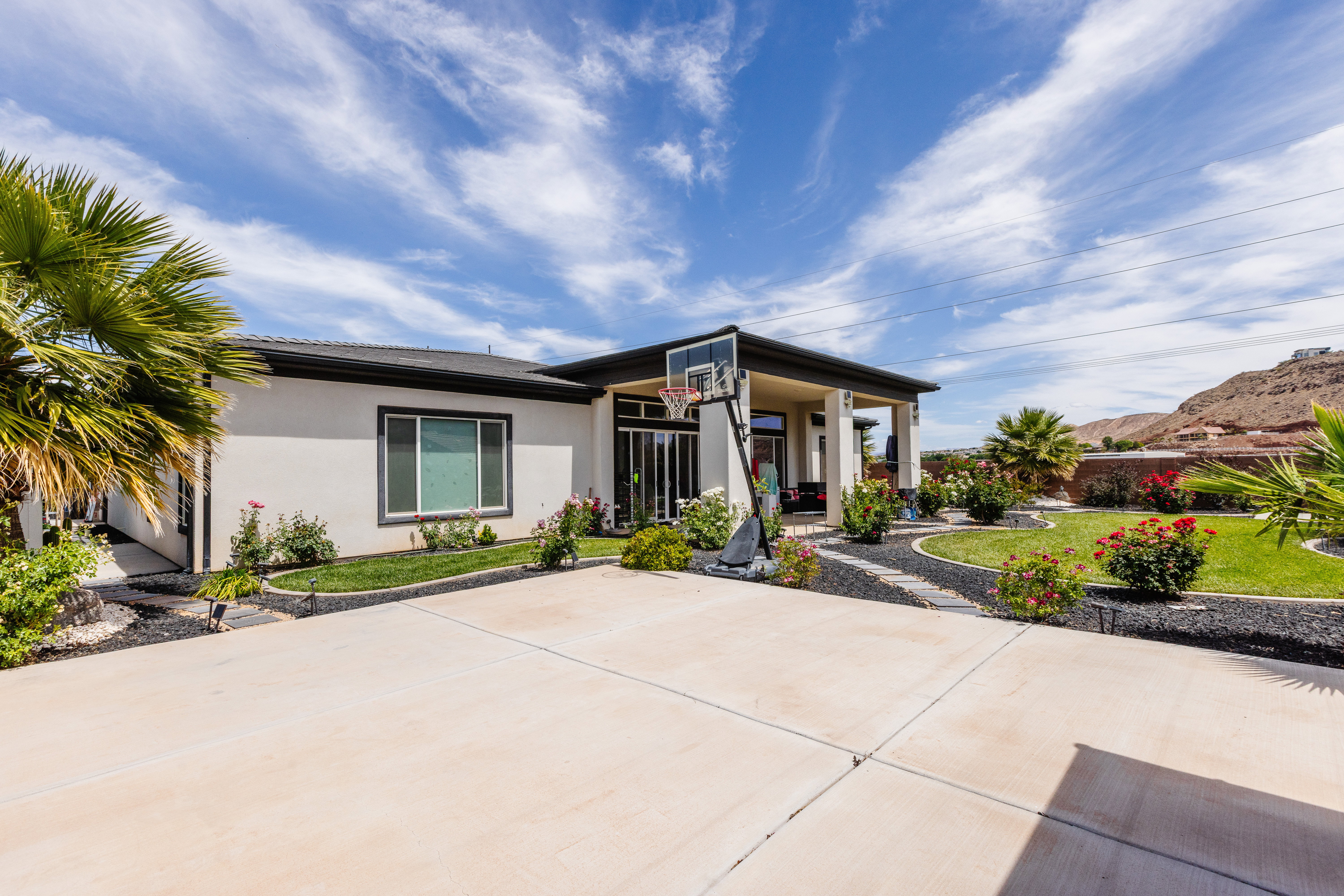 Exterior with a concrete driveway, covered patio, manicured lawn, and mature landscaping