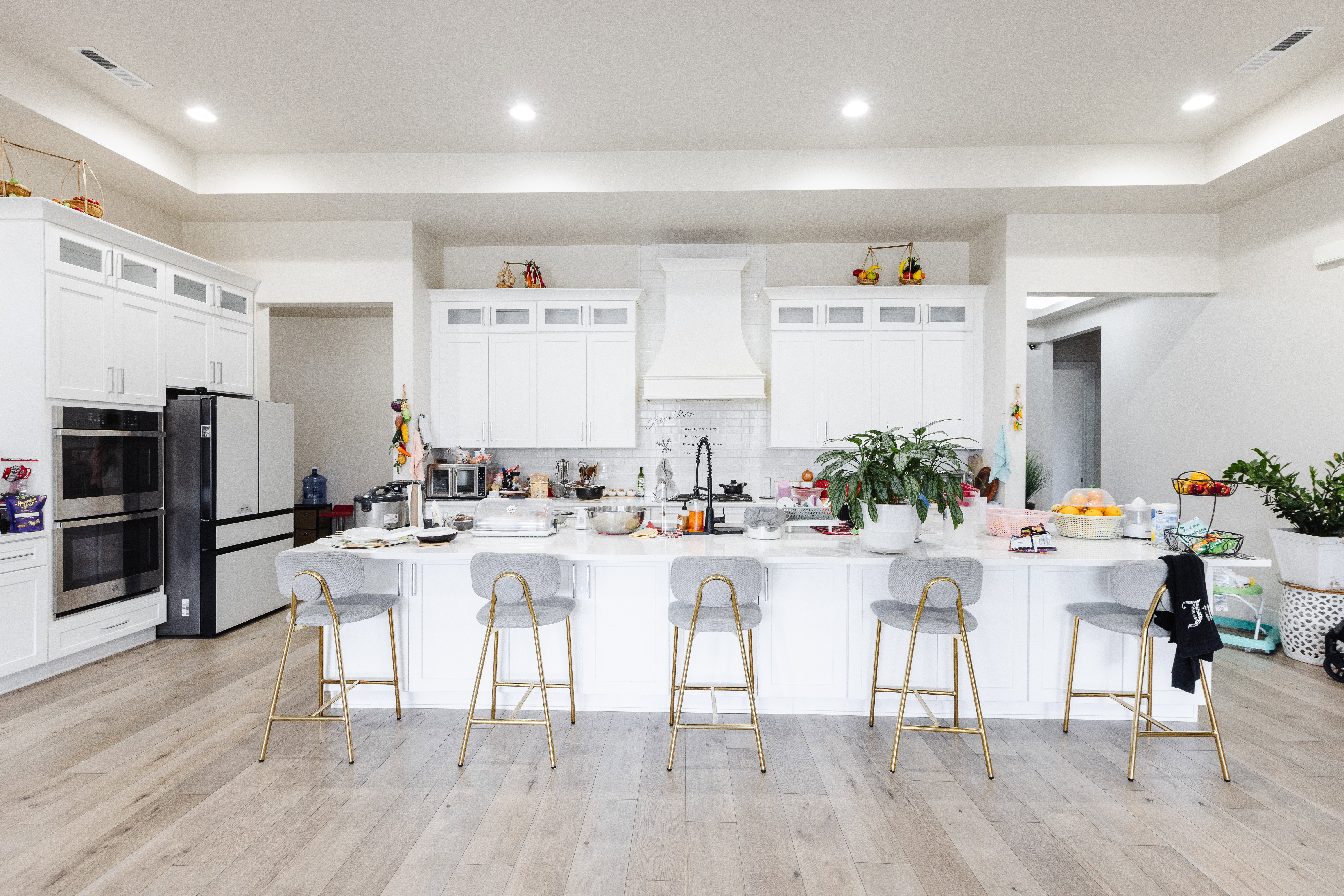 Contemporary kitchen featuring an oversized island with seating, white shaker cabinetry, recessed lighting, double wall ovens, and wood-finish flooring