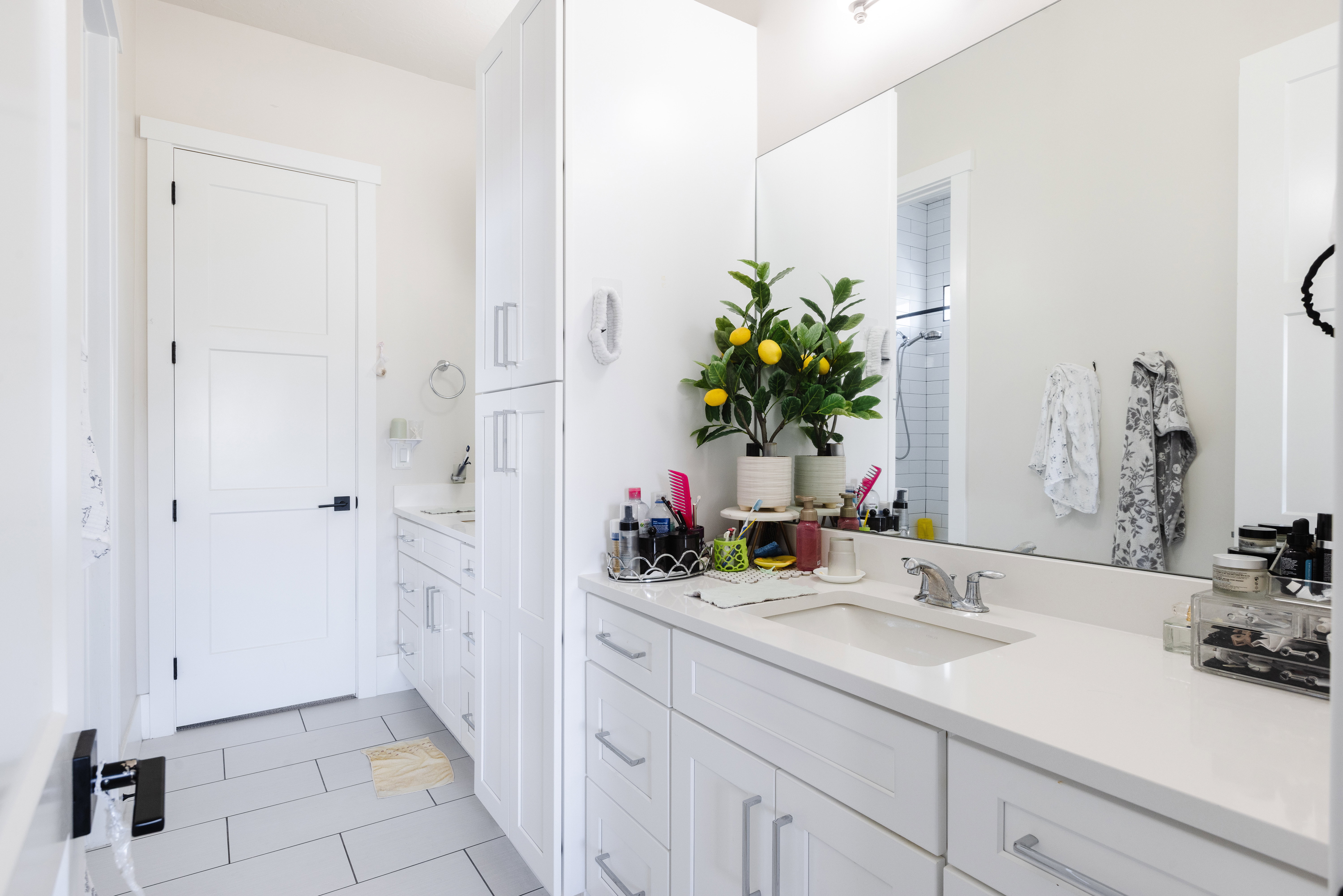 Bathroom vanity featuring dual sinks, white cabinetry, a large wall-mounted mirror, and tile flooring